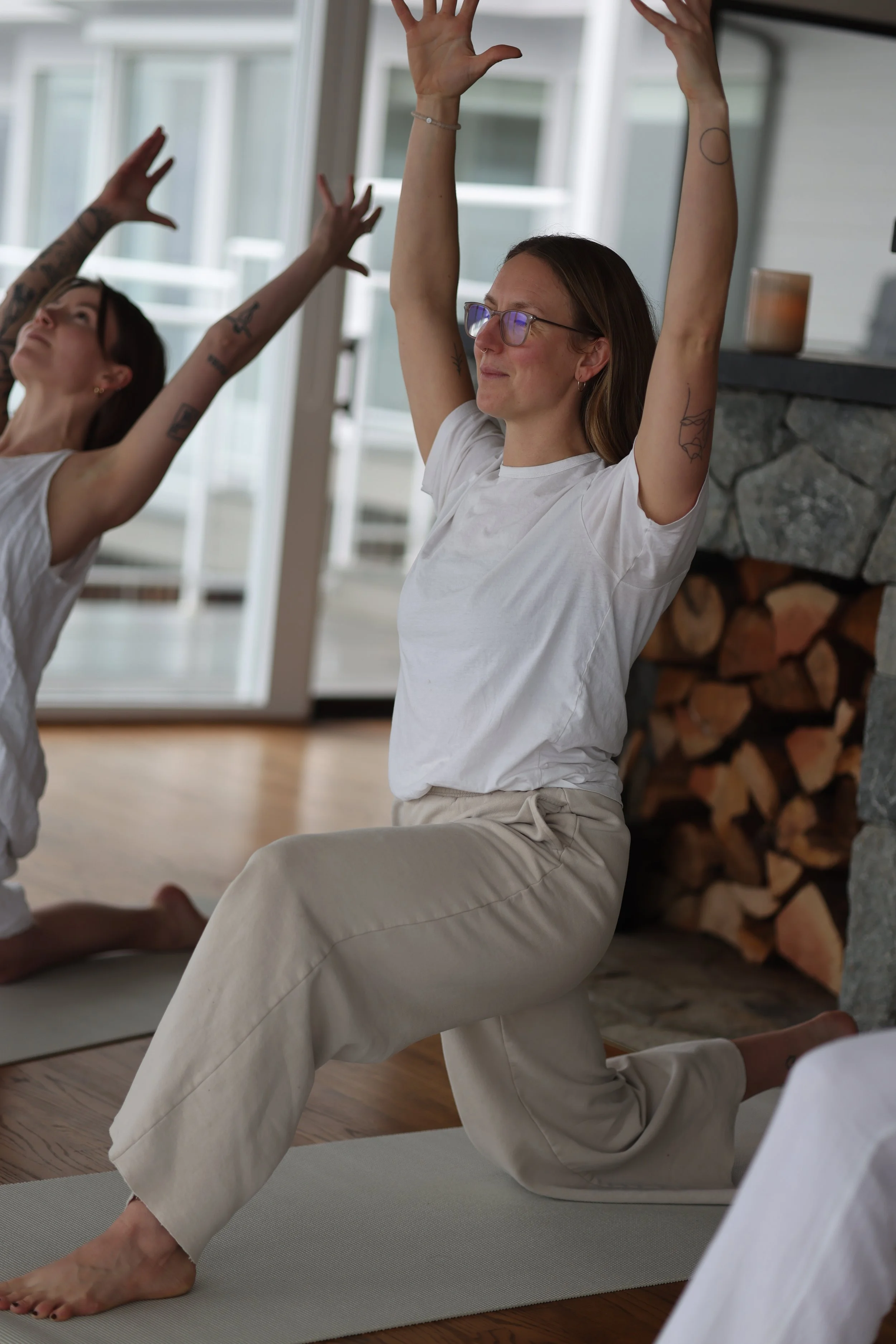 Women practicing yoga together in a cozy indoor setting, with a fireplace and large windows.