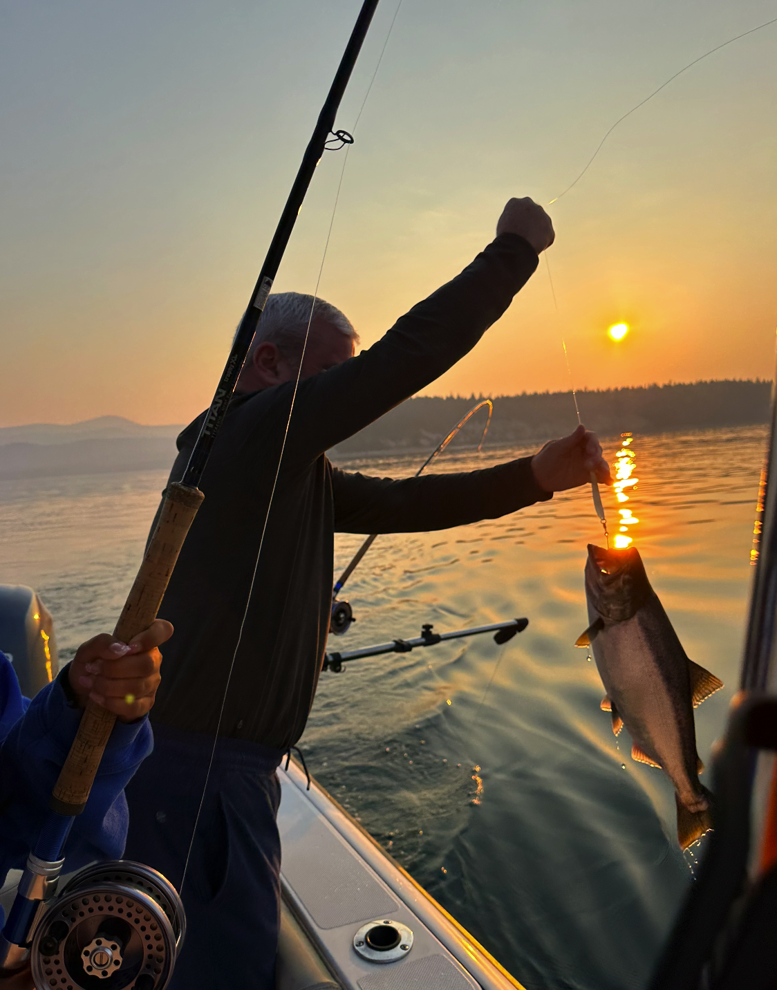 Person holding a fishing rod and a fish during sunset on a boat.