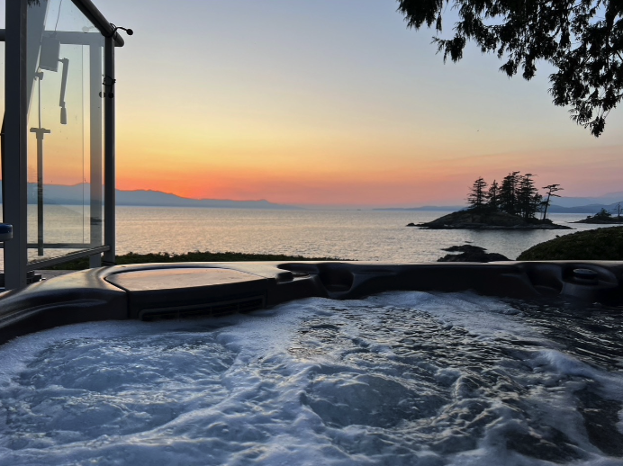Hot tub with bubbling water overlooking ocean sunset and distant trees on small island.