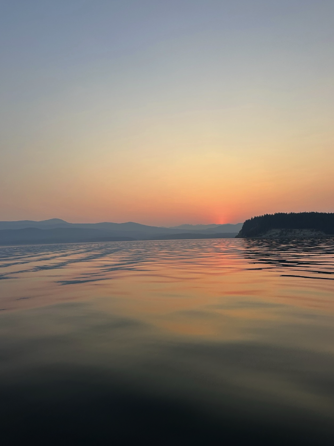Calm lake during sunset with pink and orange hues in the sky and distant mountains on the horizon.