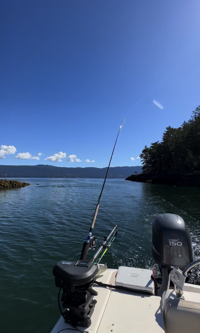 View from a boat showing a fishing rod mounted on the boat, a Yamaha 150 outboard motor, and calm water with distant islands and a partly cloudy sky.