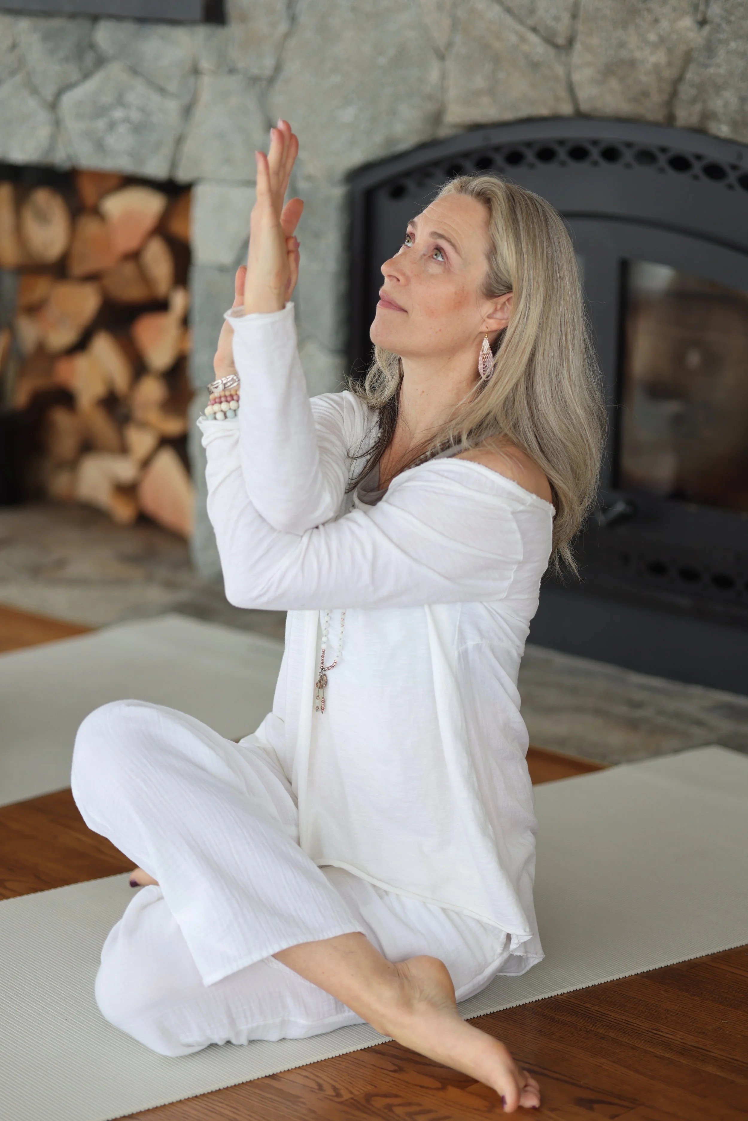 A woman practicing yoga or meditation on a yoga mat in a cozy room with a stone fireplace.