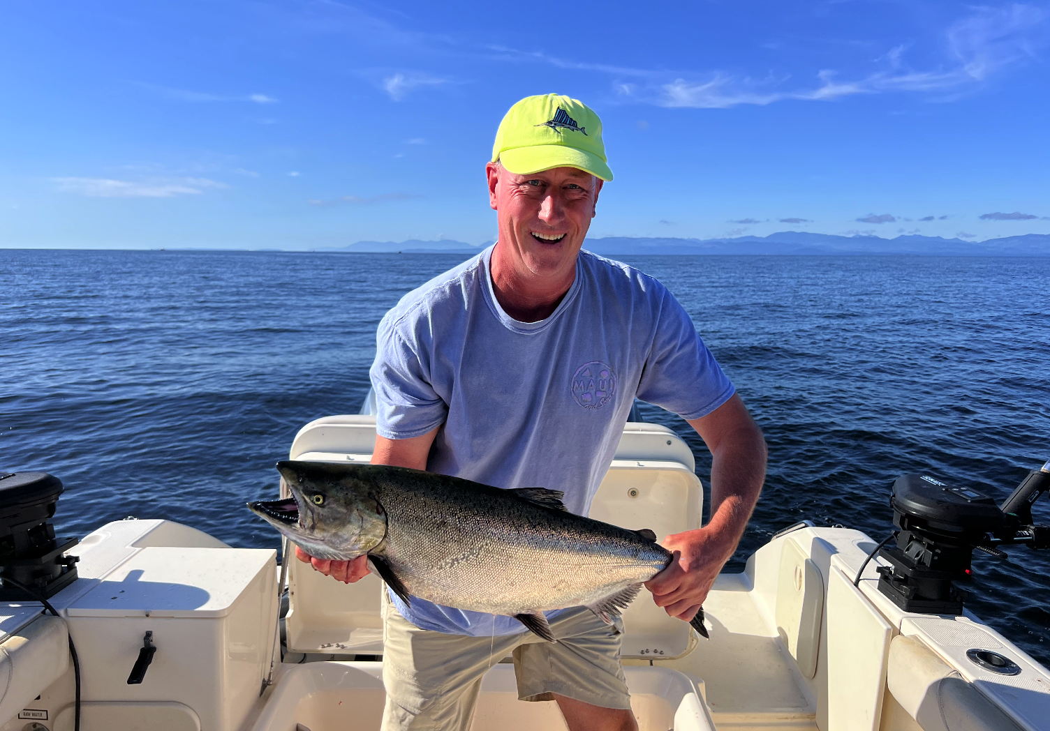 A man smiling and holding a large fish on a boat in the ocean under a blue sky.