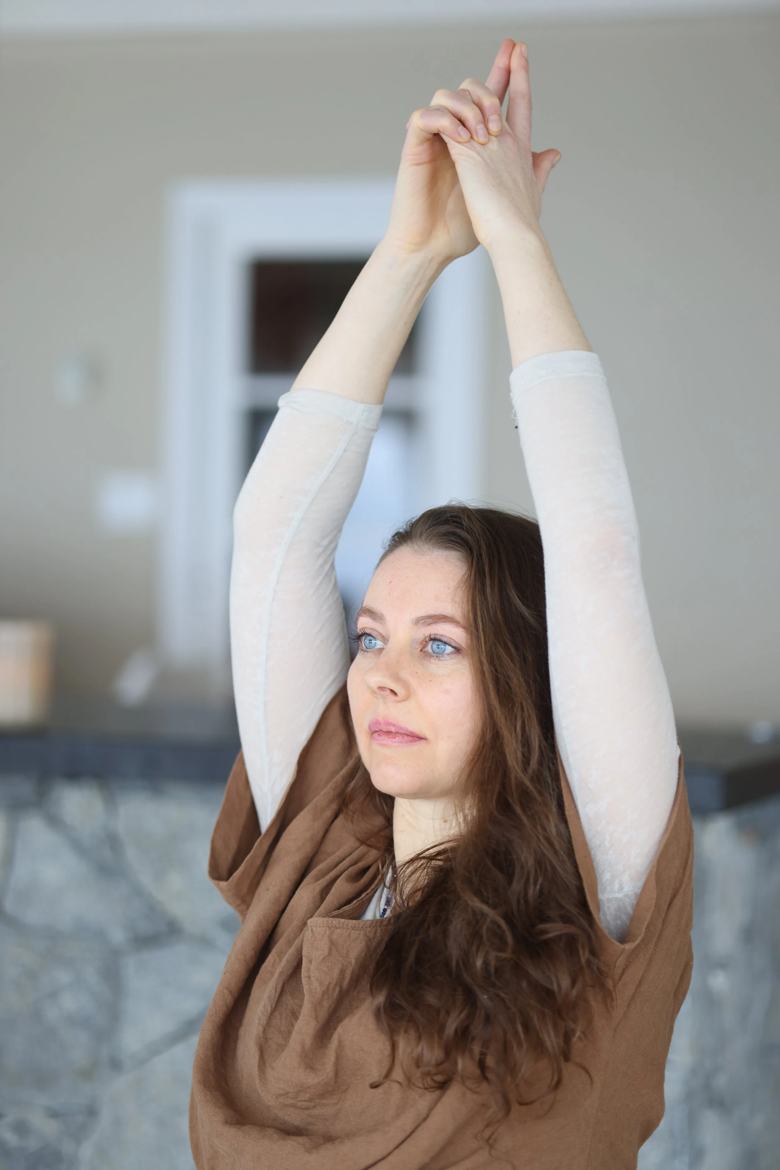 A woman stretching her arms overhead while seated indoors.