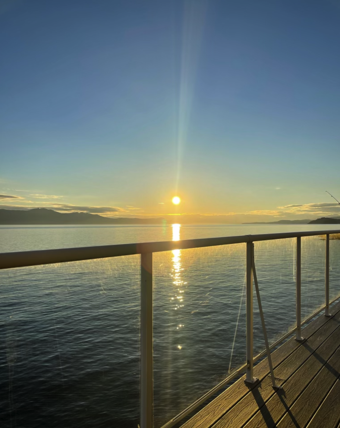 A scenic view of a sunrise over a body of water seen from a wooden boardwalk with a metal railing.