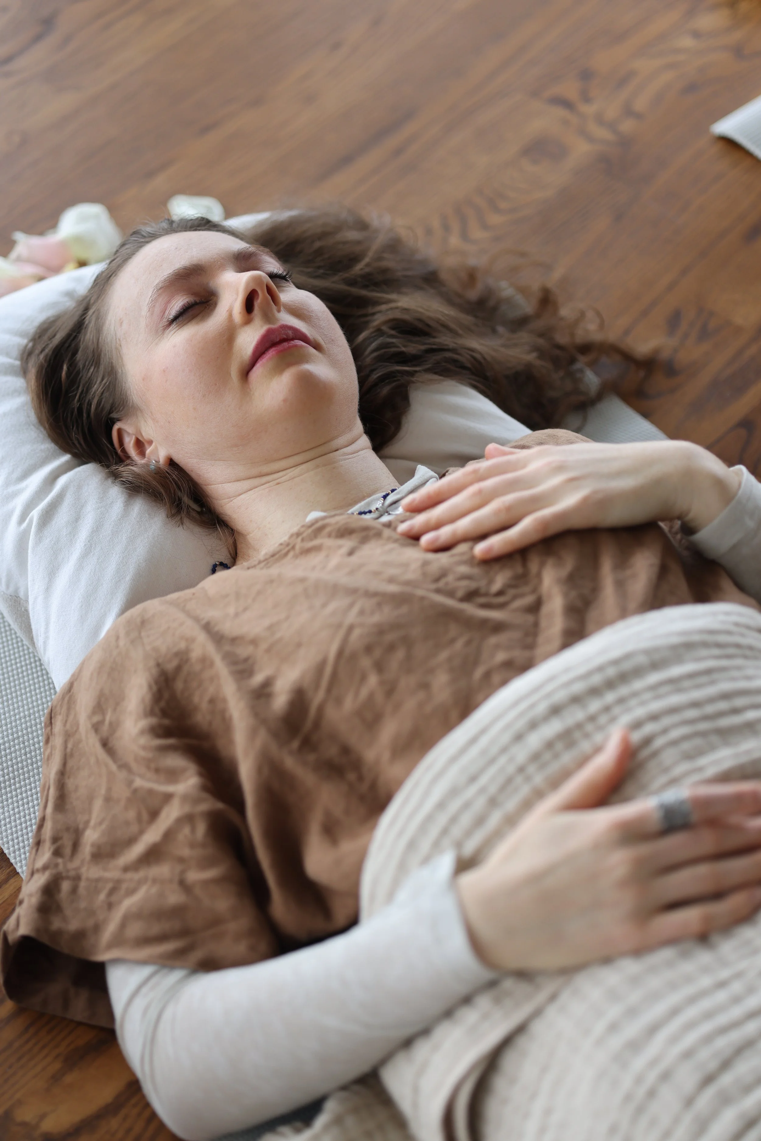 A woman lying down with eyes closed on a pillow, resting on a wooden floor.