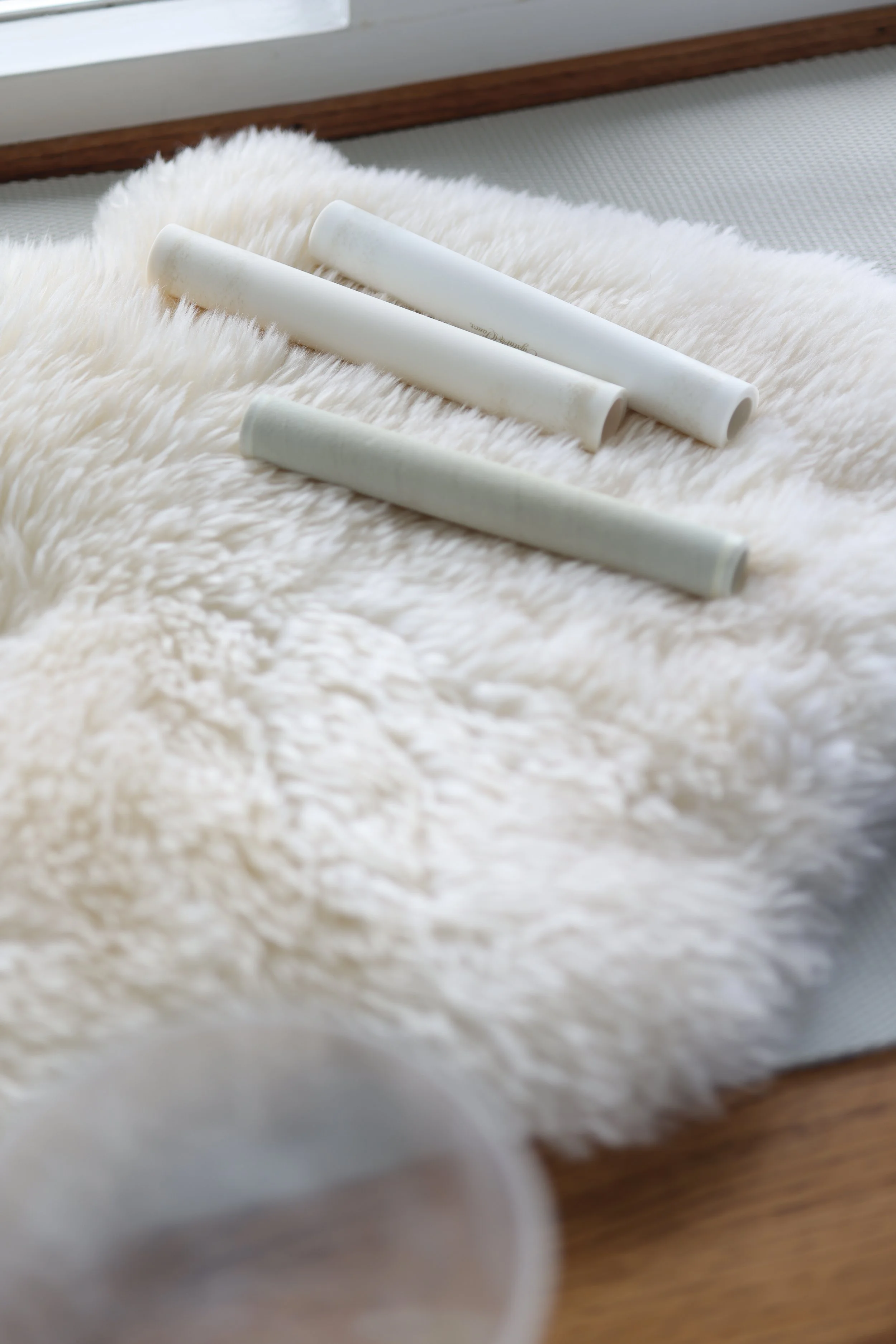 Three white chalk sticks placed on a soft, cream-colored, fluffy fur rug.