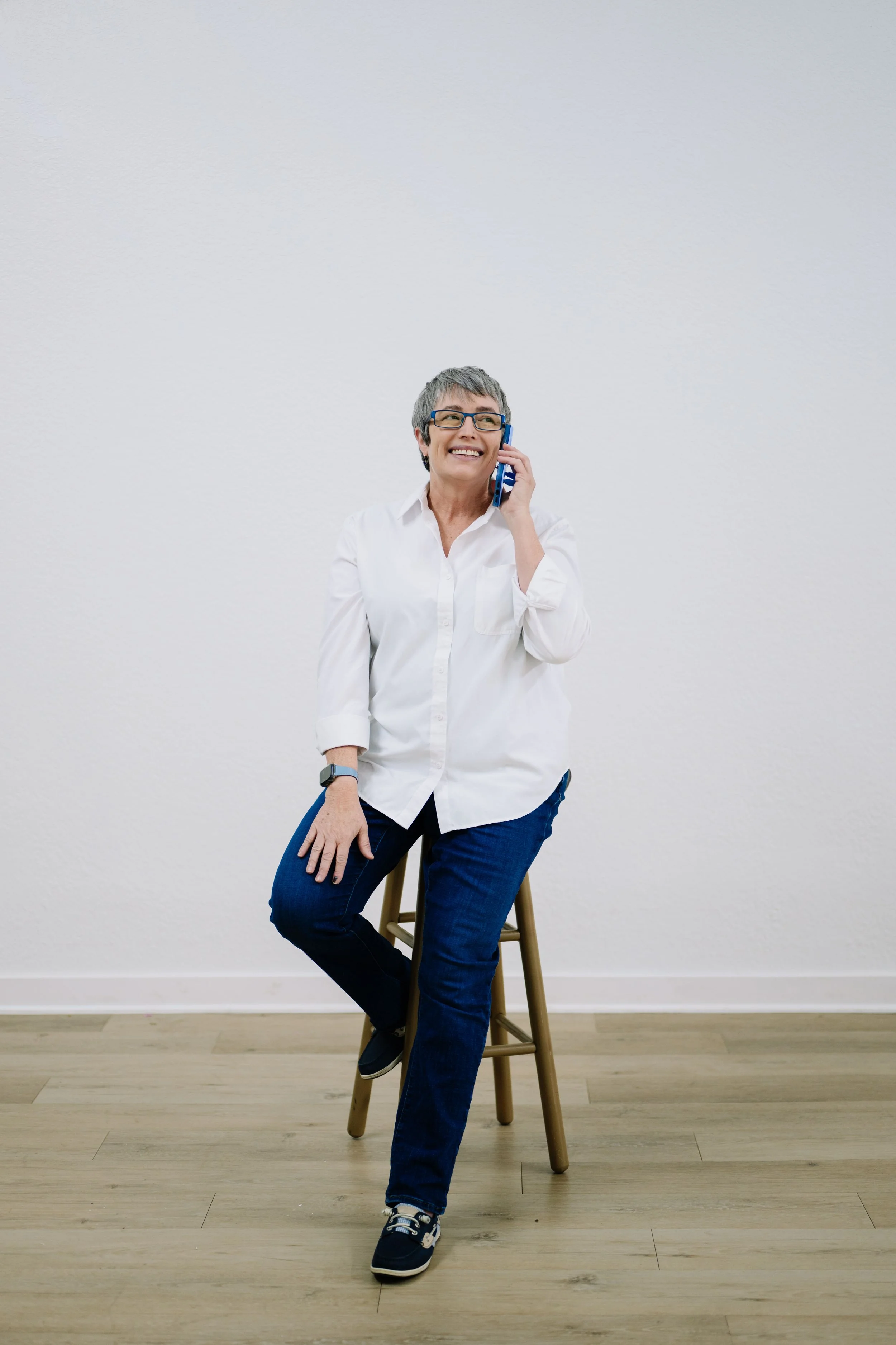 Cindi in white top sitting on stool talking on phone looking off into the distance