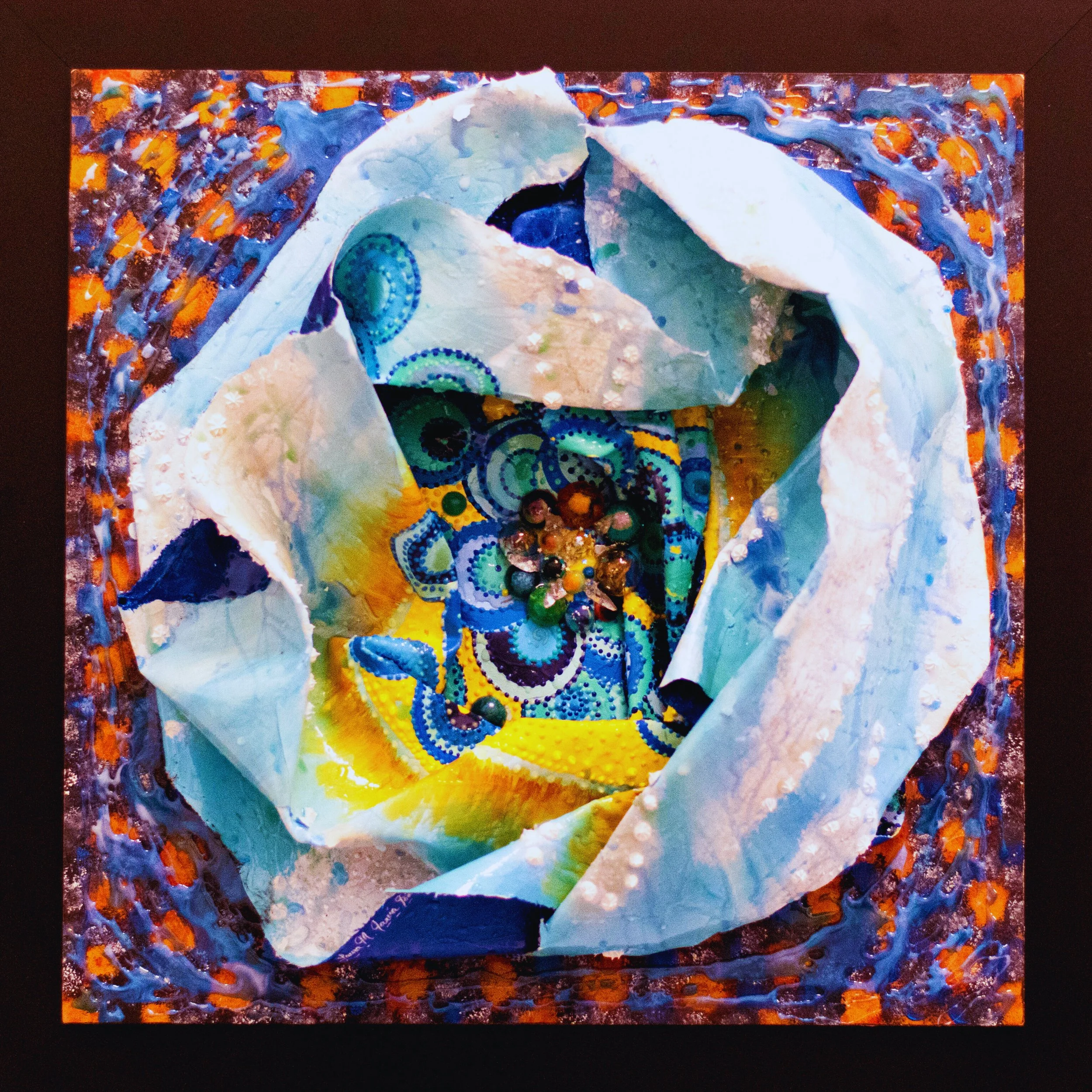 “Textured mixed media artwork with folded white fabric structure revealing colorful circular patterns and bead details in a cosmic abstract composition.”