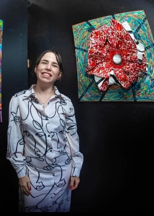 The artist Laura M. Garcia Gordo posing in front of her art, Black Hole Fire Element. “Vibrant abstract black hole artwork with explosive red central structure and radiating energetic lines representing the fire element.”