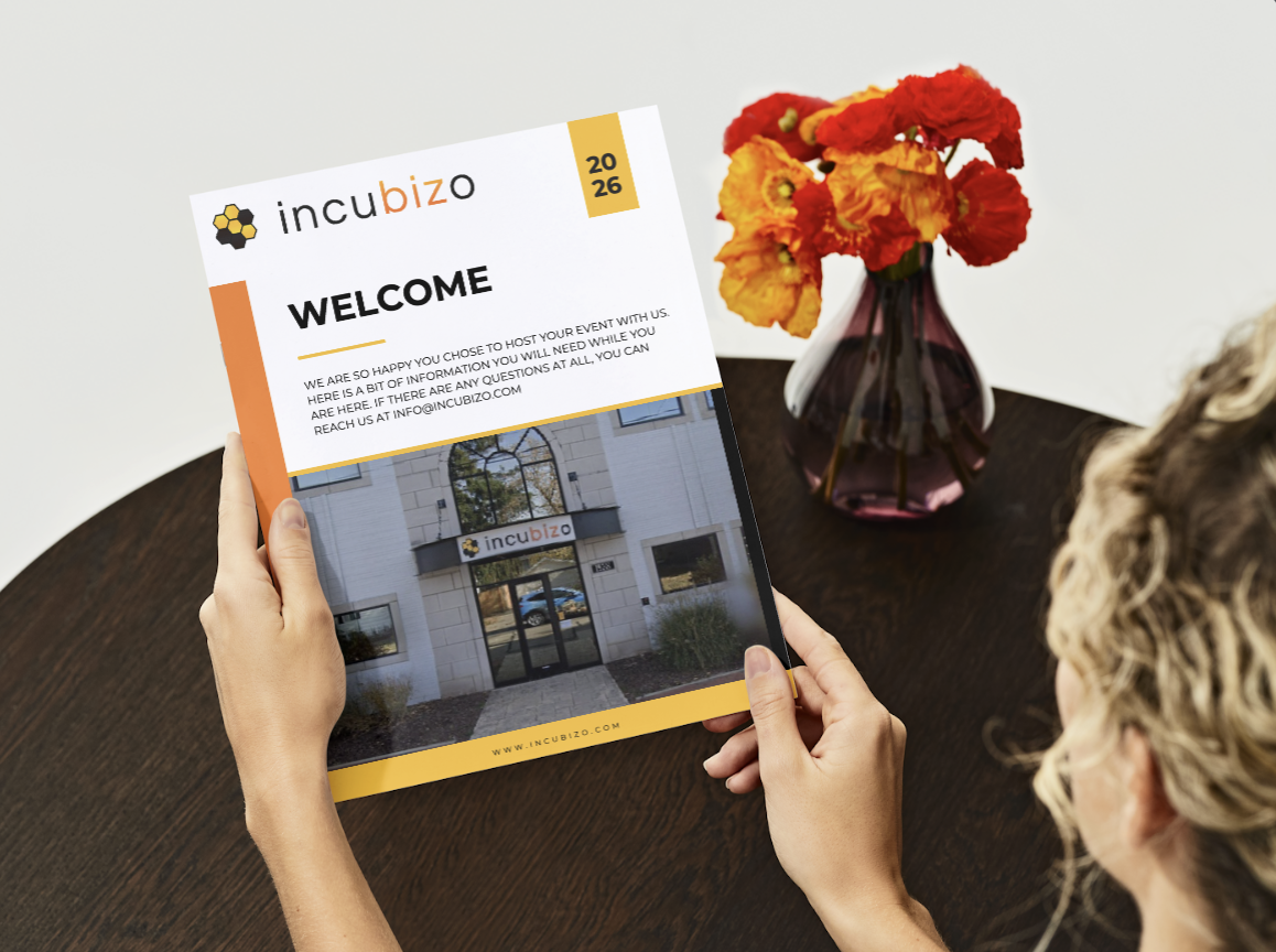 Person holding a flyer with Incubizo logo, welcoming text, and a photo of the Incubizo building on the flyer, placed on a dark wooden table next to a vase with red and yellow flowers.