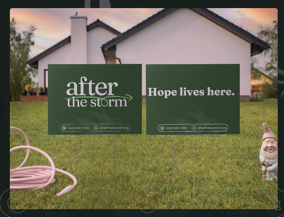 Two yard signs in front of a house with the messages "after the storm" and "Hope lives here."" The house is white with black roof, and the yard has green grass. Garden gnome and pink garden hose are on the lawn.