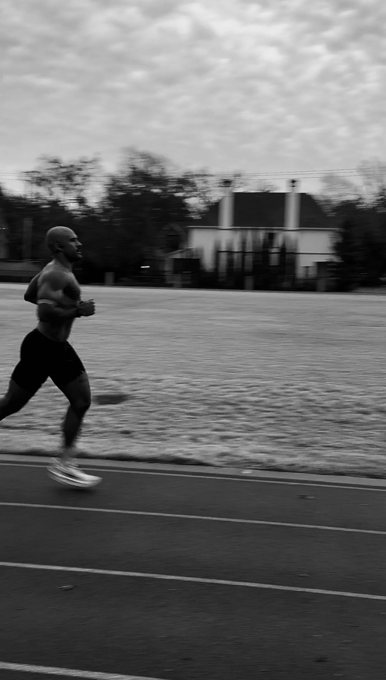 A man jogging on a track in a black and white photo, with houses and trees in the background.