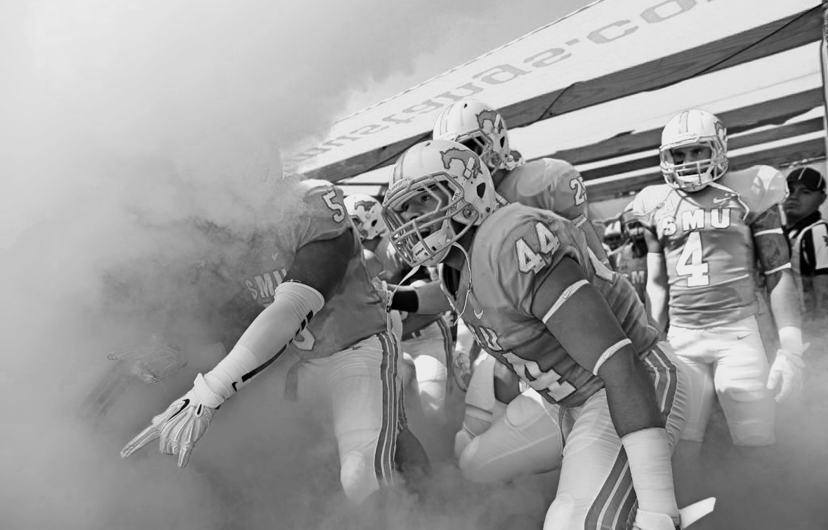 Football players entering the field through a cloud of smoke