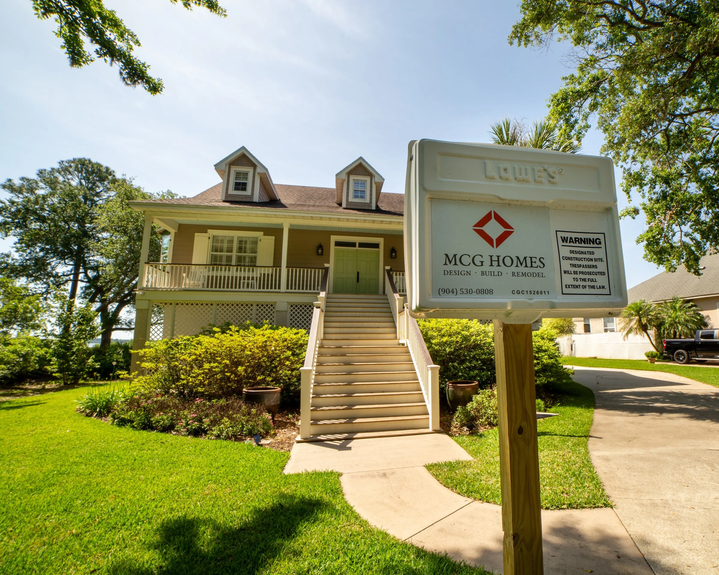 MCG Homes construction site sign in front of a raised coastal cottage with dormer windows and a green front door.
