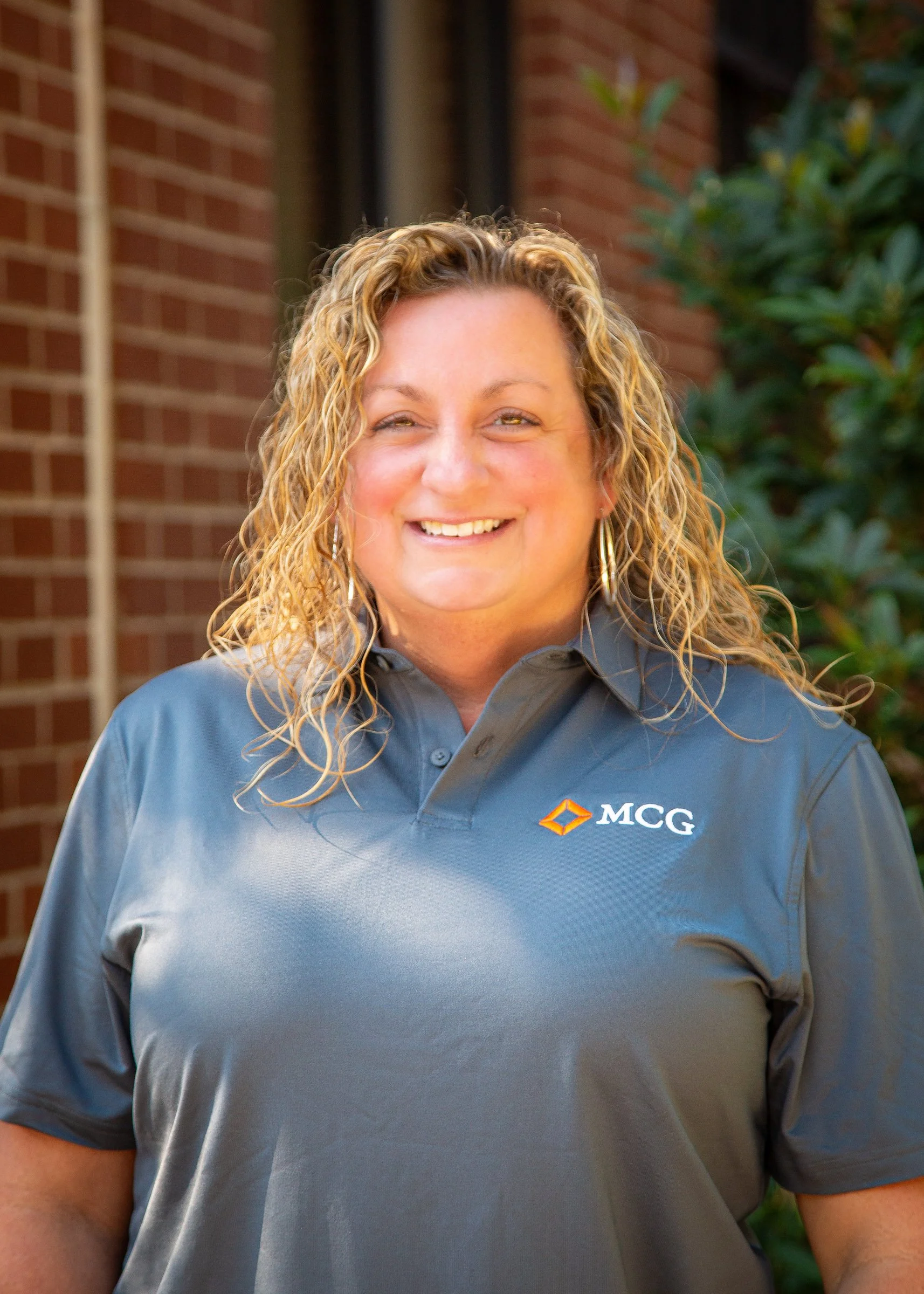 A woman smiling for a photo with a brick wall in the background.