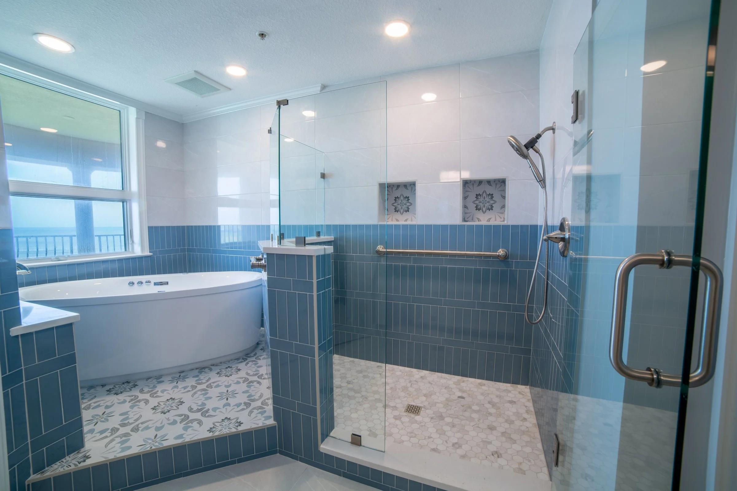 Coastal bathroom with freestanding tub, blue subway tile, and glass walk-in shower overlooking the ocean