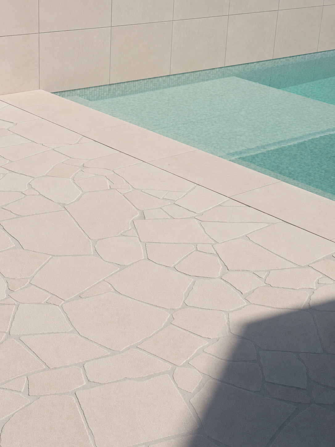 A close-up of a textured beige outdoor patio near a swimming pool with beige tiled walls.