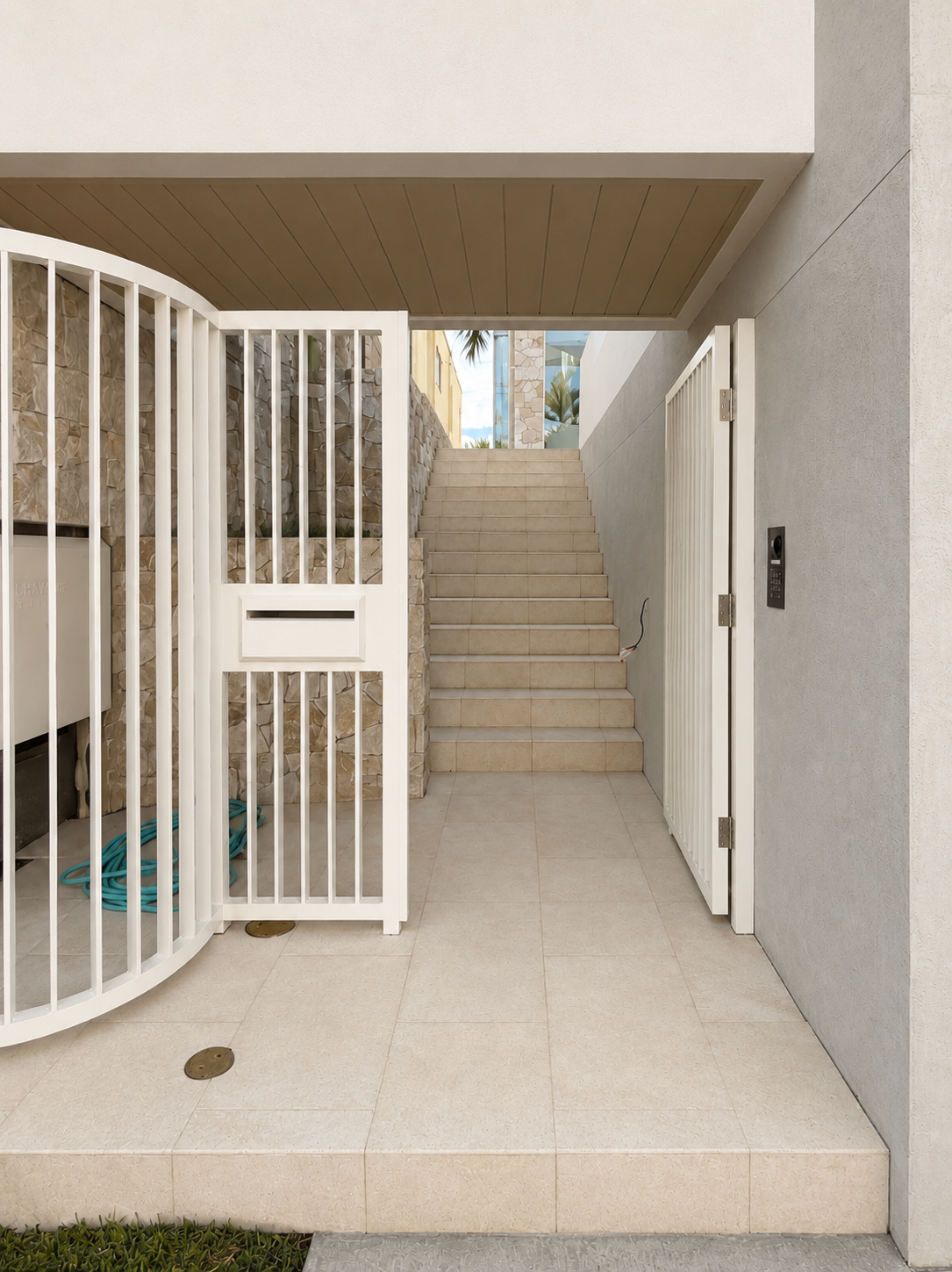 Modern apartment building entrance with steps leading up, a white curved gate, stone wall, and electrical panel.