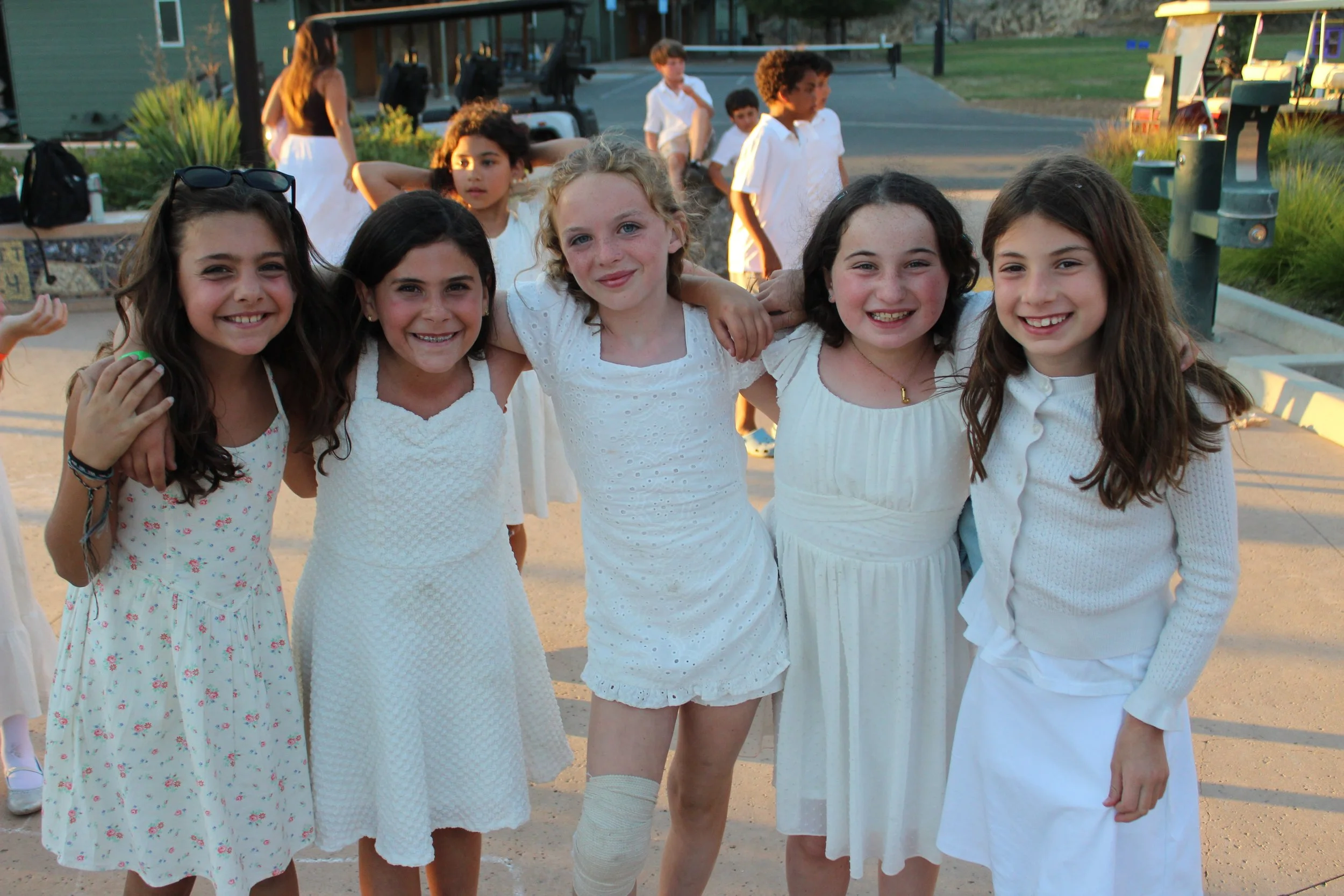 Group of young girls dressed in white at an outdoor event during sunset.