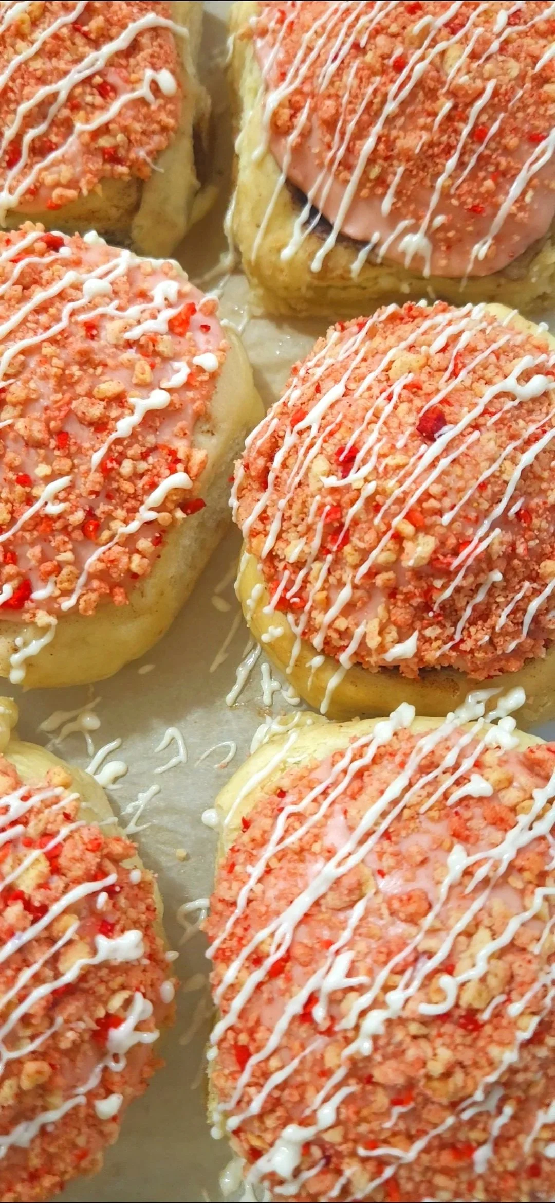 Close-up of six sweet rolls with crumbled strawberry vanilla cookie topping and white drizzle.