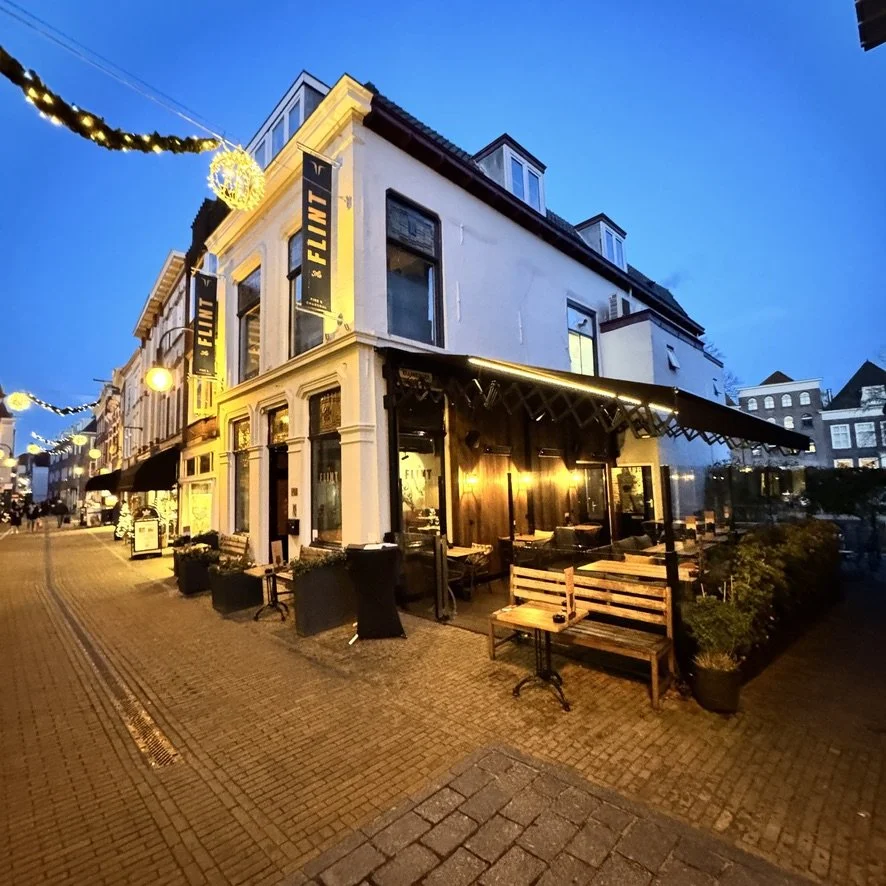 Uitgaansgebied met verlichte cafés en winkels, straatverlichting, en een gezellige sfeer in de avond in een Europese stad.