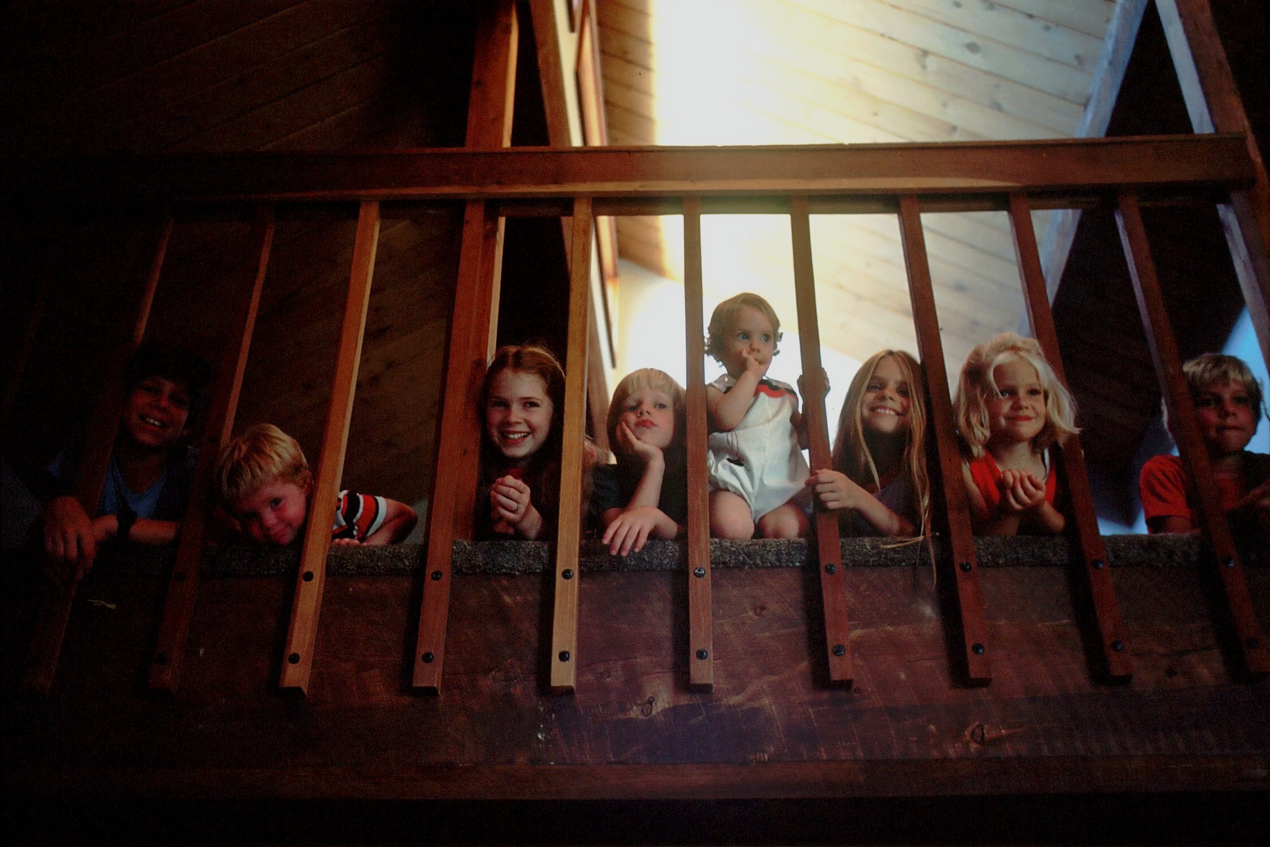 Image of 7 children peeking through staircase smiling