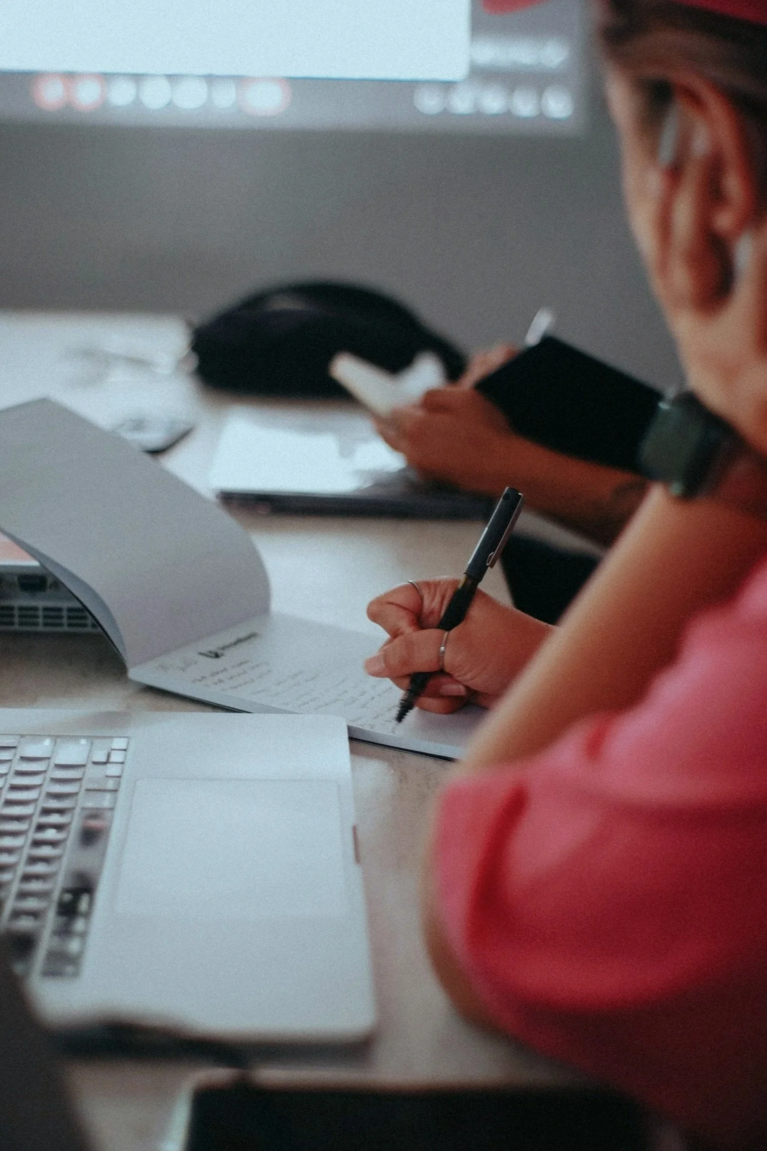 Image of a person working on a laptop at a desk and writing in a notebook