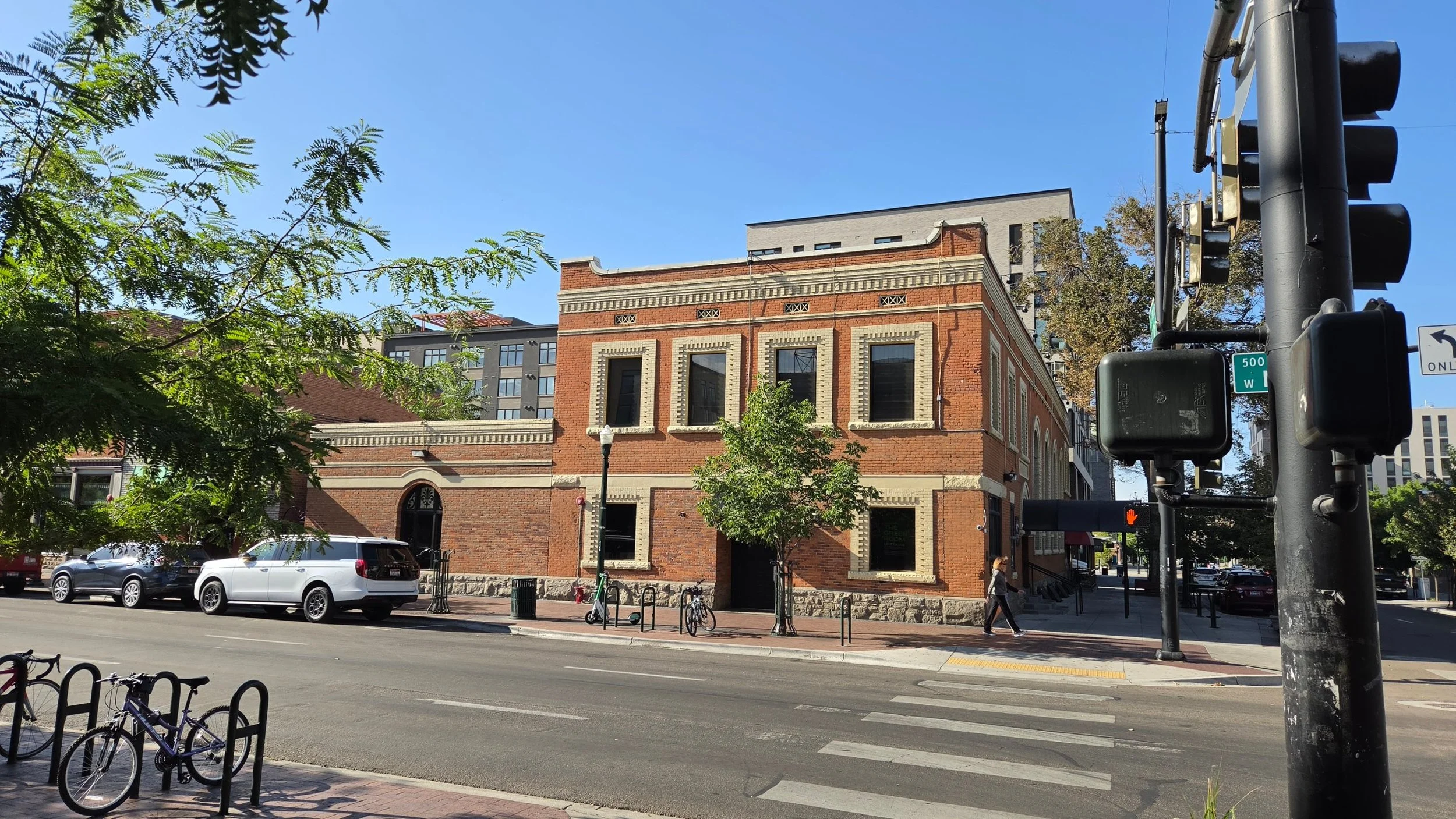 Historic two-story red brick commercial building with cream stone trim and a rusticated stone base at a downtown Boise, Idaho street corner, with newer mid-rise buildings behind