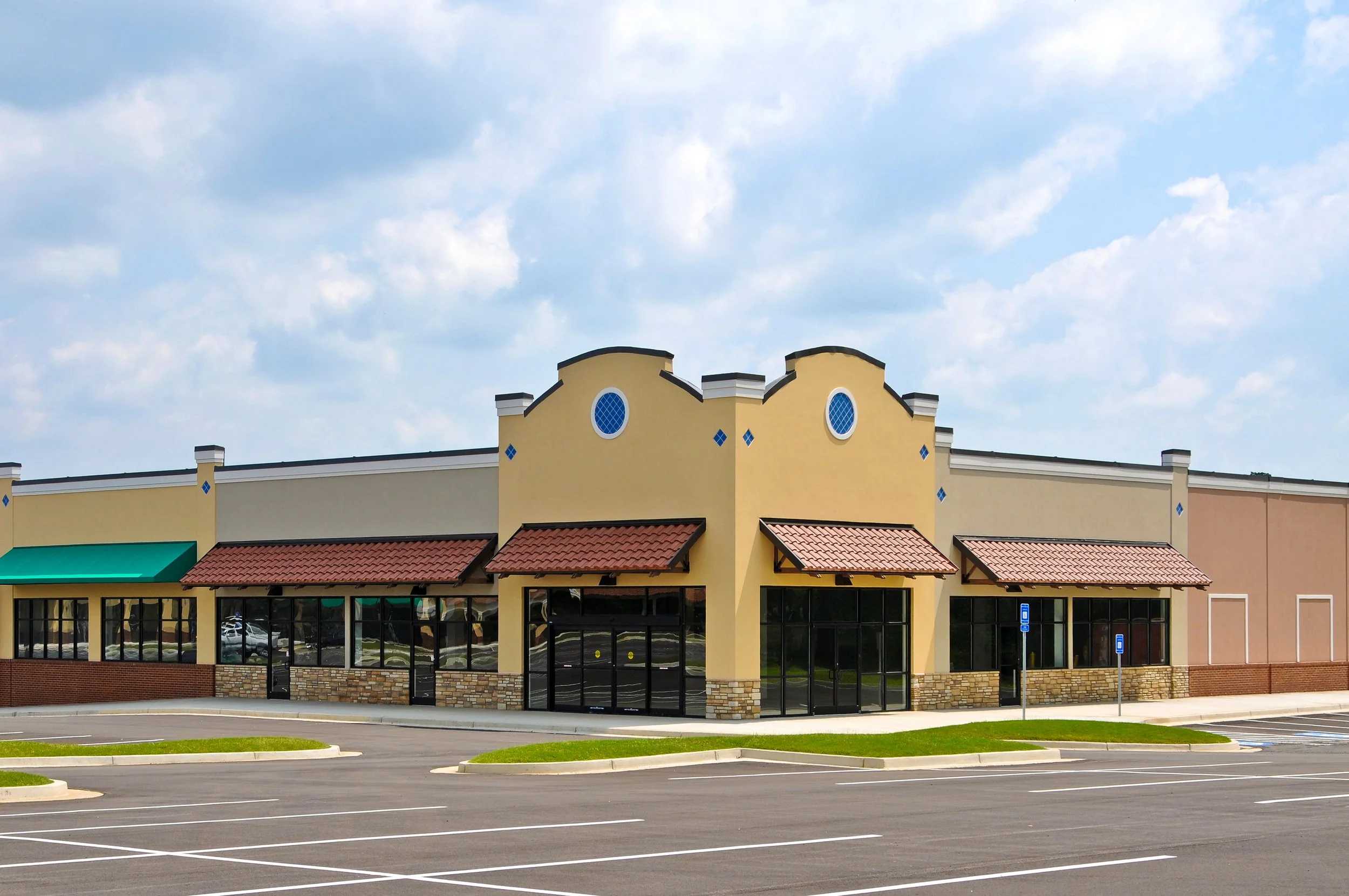 Vacant storefront in a strip mall with parking lot, clear sky background.