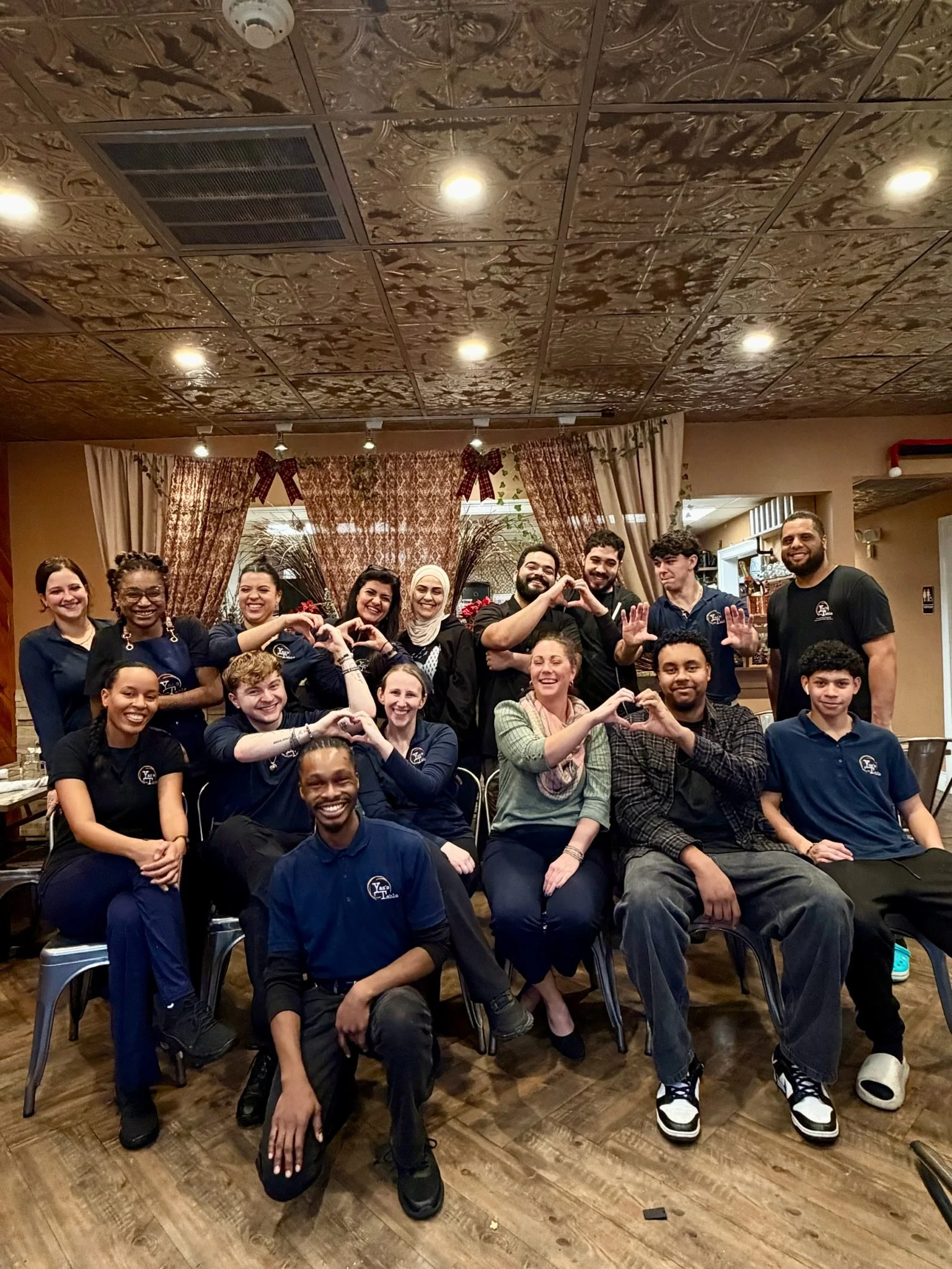 A group of diverse people in a restaurant posing for a photo, some making heart shapes with their hands.