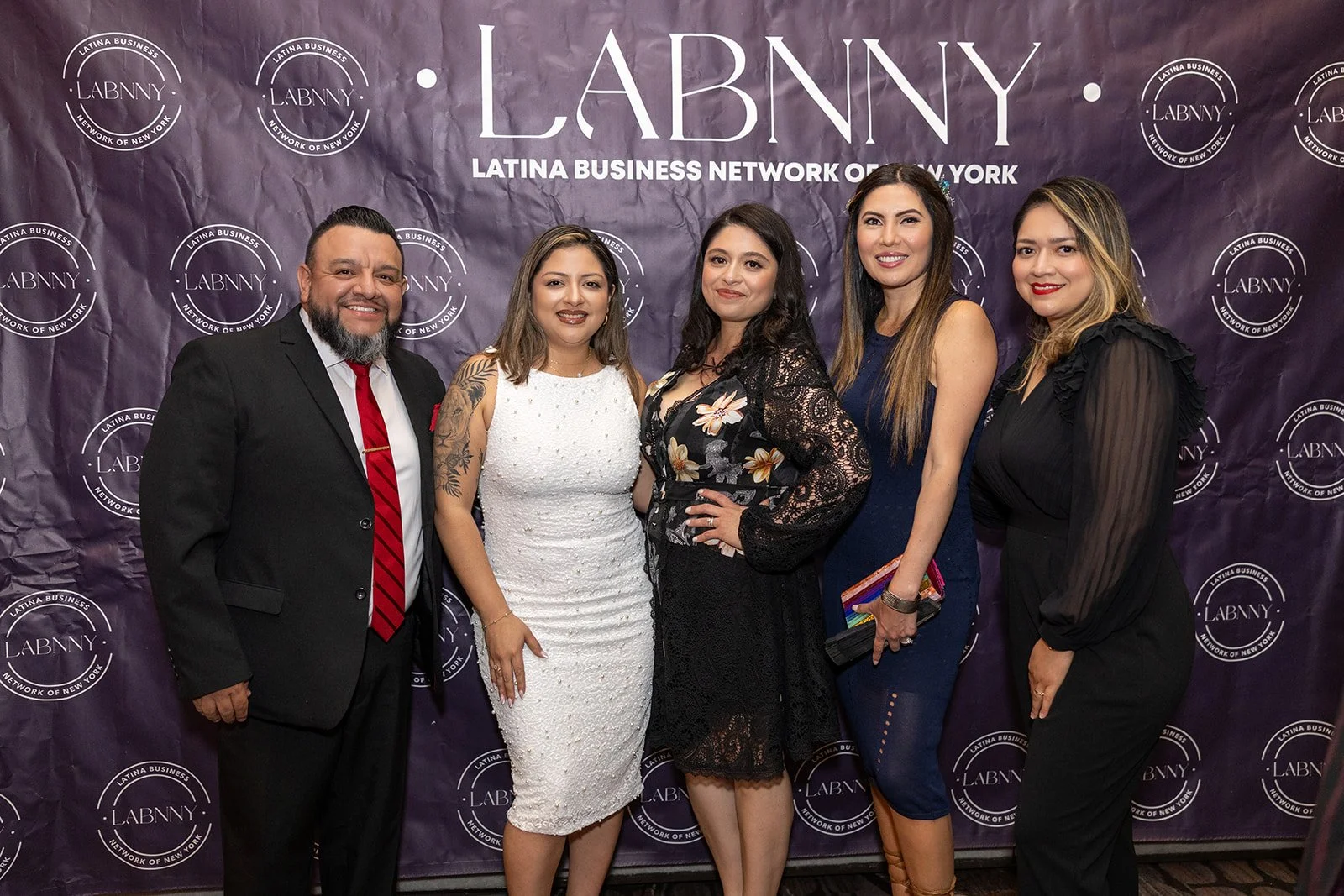 Six people standing together in front of a purple background with the LABNNY logo, all dressed in formal attire and smiling at the camera.