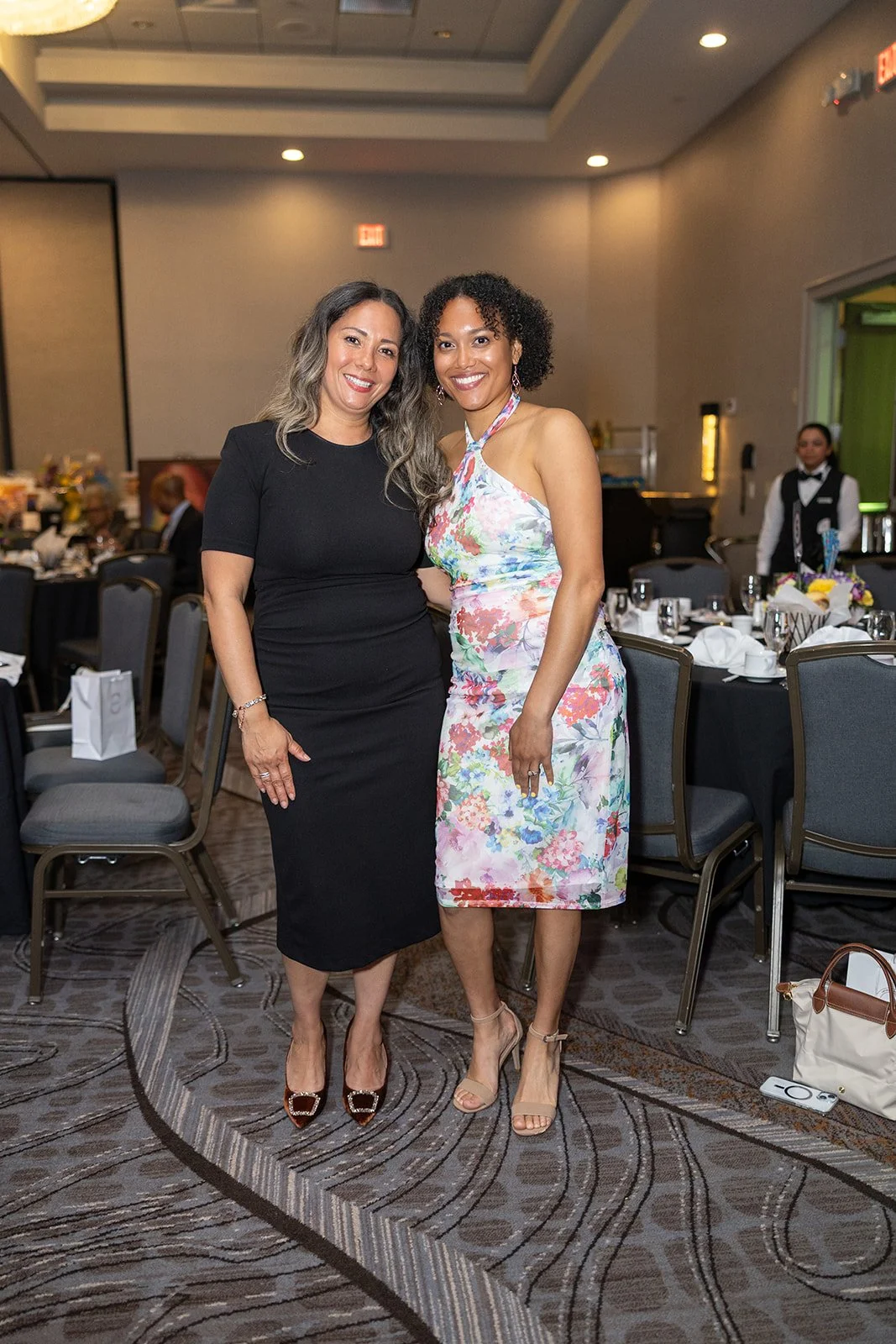 Two women standing together in formal attire at a banquet hall, smiling at the camera.