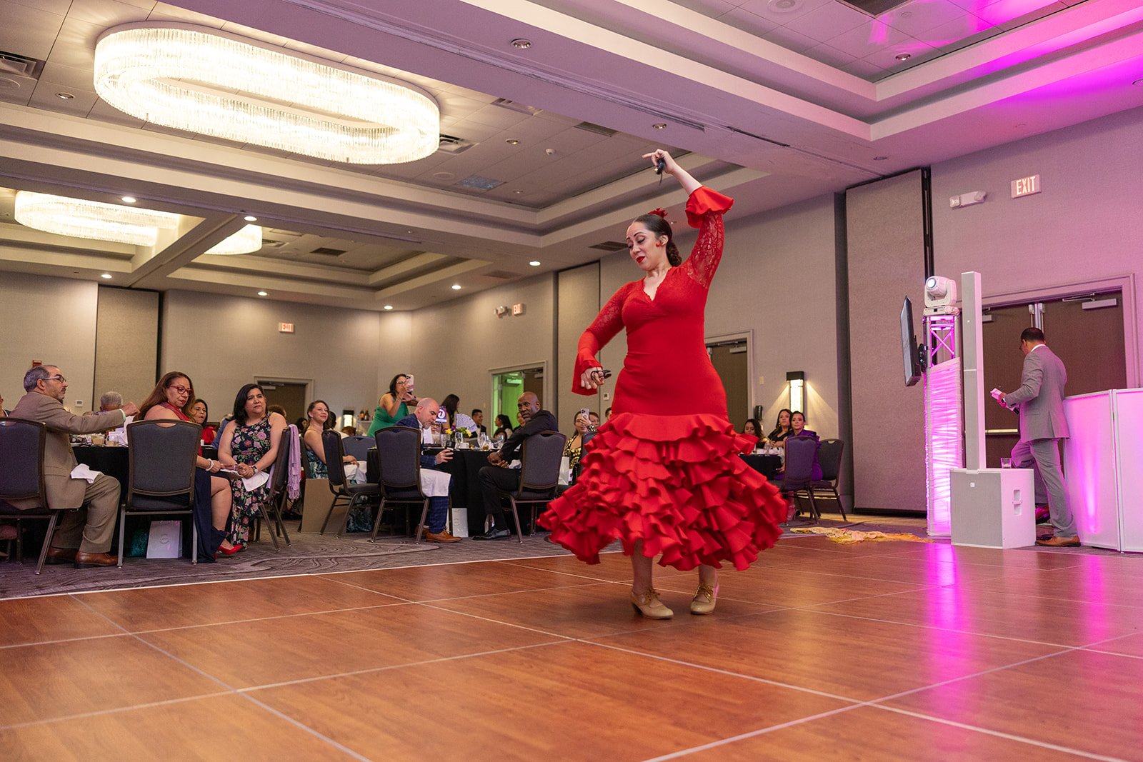 Woman in red flamenco dress dancing on a wooden floor at an event.