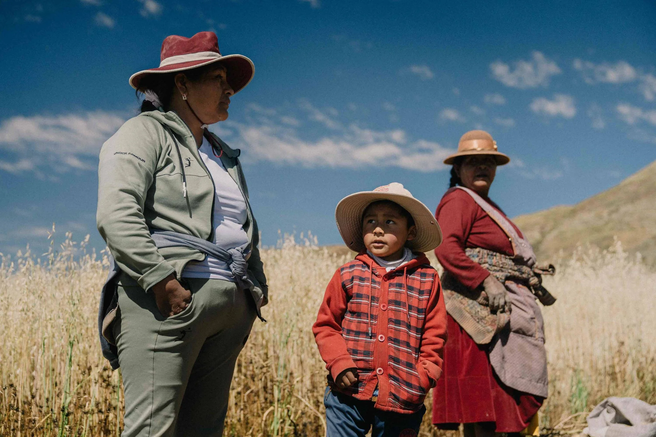 A portrait of two local women and a young boy from a community near Lake Titicaca, Peru, standing in golden wheat fields.
