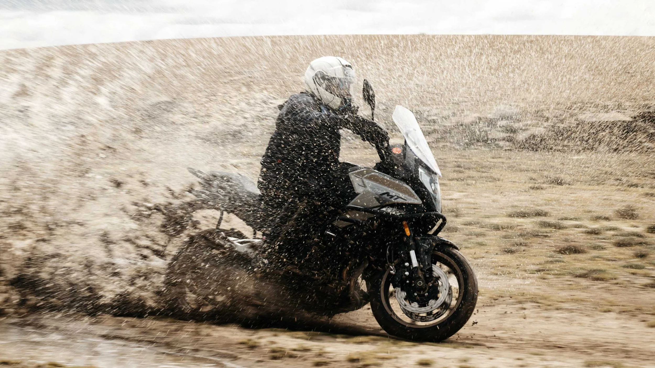 Slow shutter action shot of a CF Moto bike creating a dramatic water splash in a puddle in Peru.