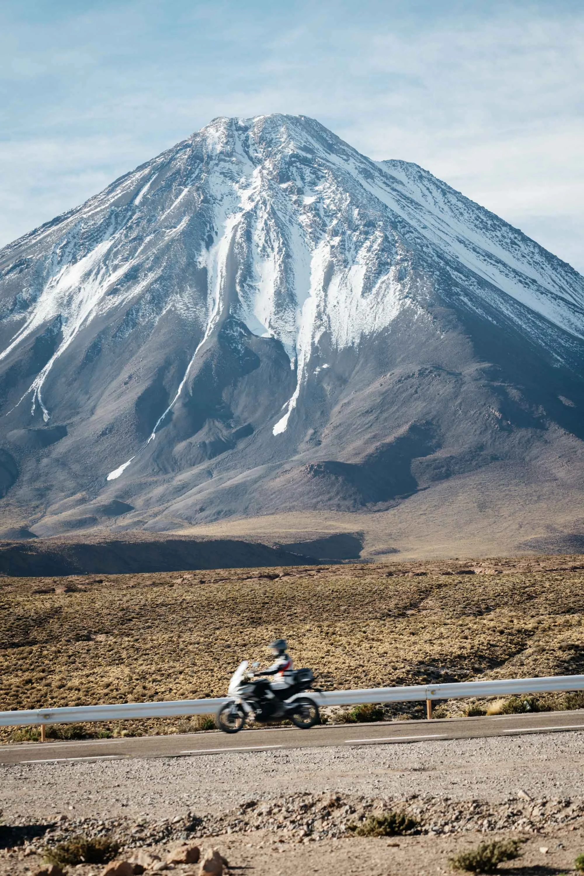 Slow shutter photography of a CF Moto rider passing the impressive Licancabur Volcano in Chile.
