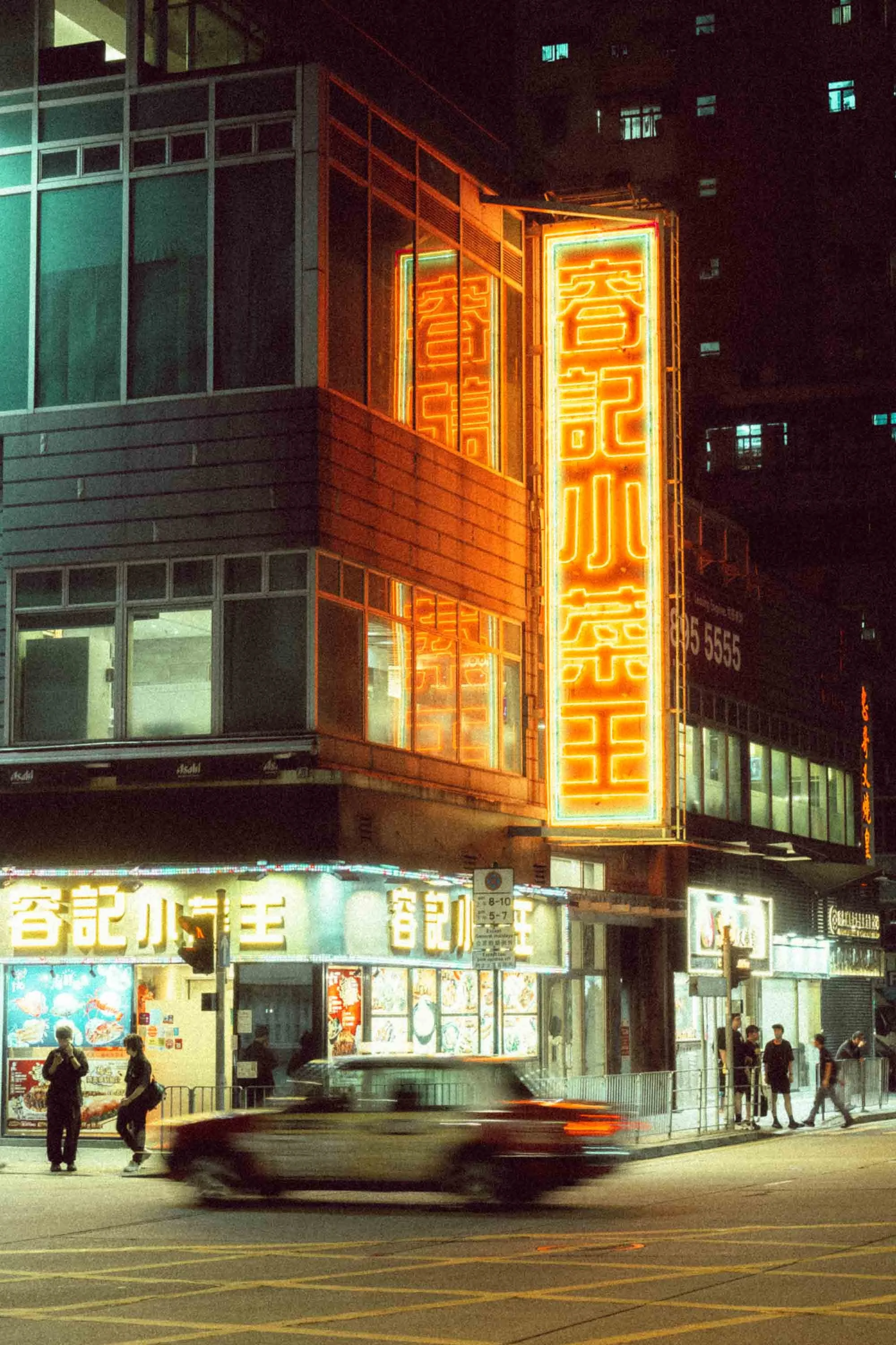Long exposure night street photo in Hong Kong capturing the light trails of a passing car against a backdrop of neon signs.