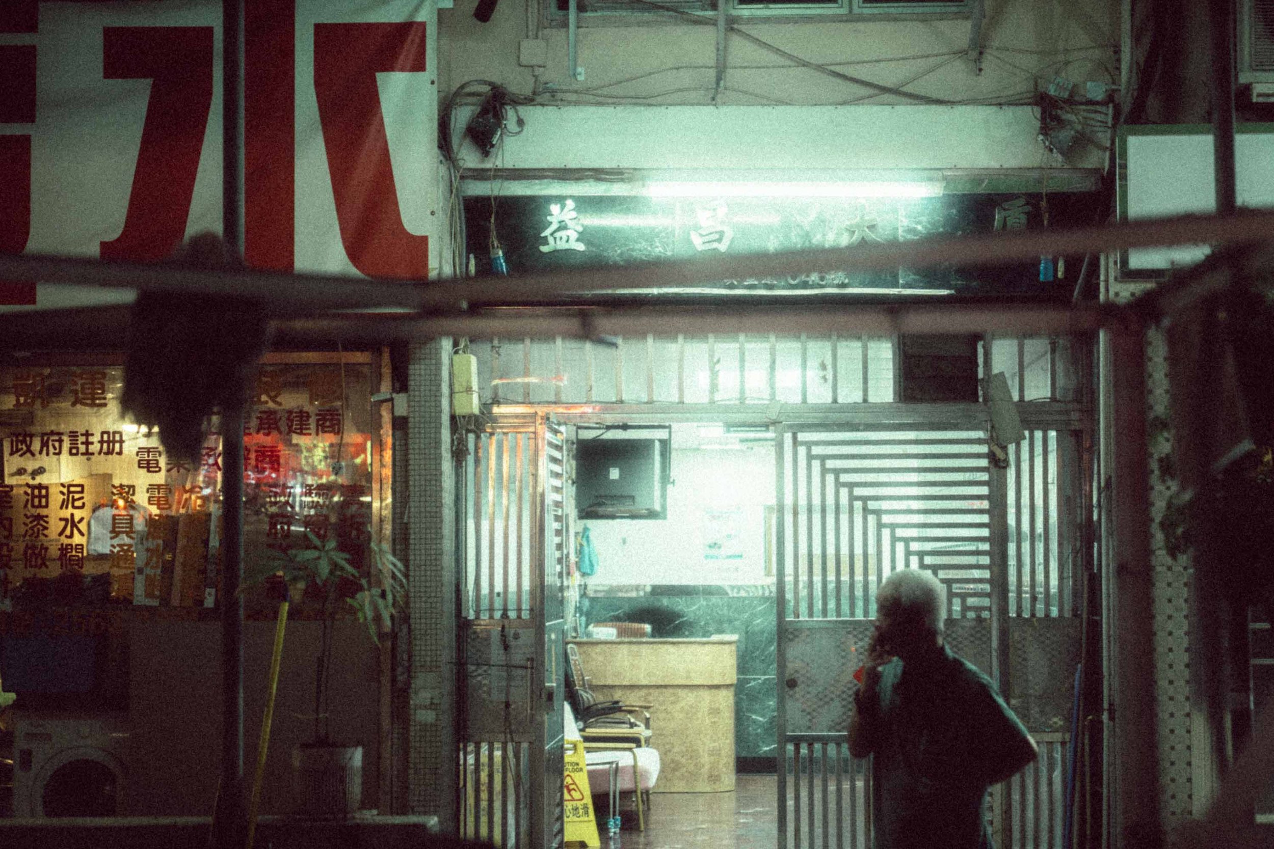 Gritty night street portrait of an old man smoking a cigarette in Hong Kong, illuminated by the glow of neon signs.