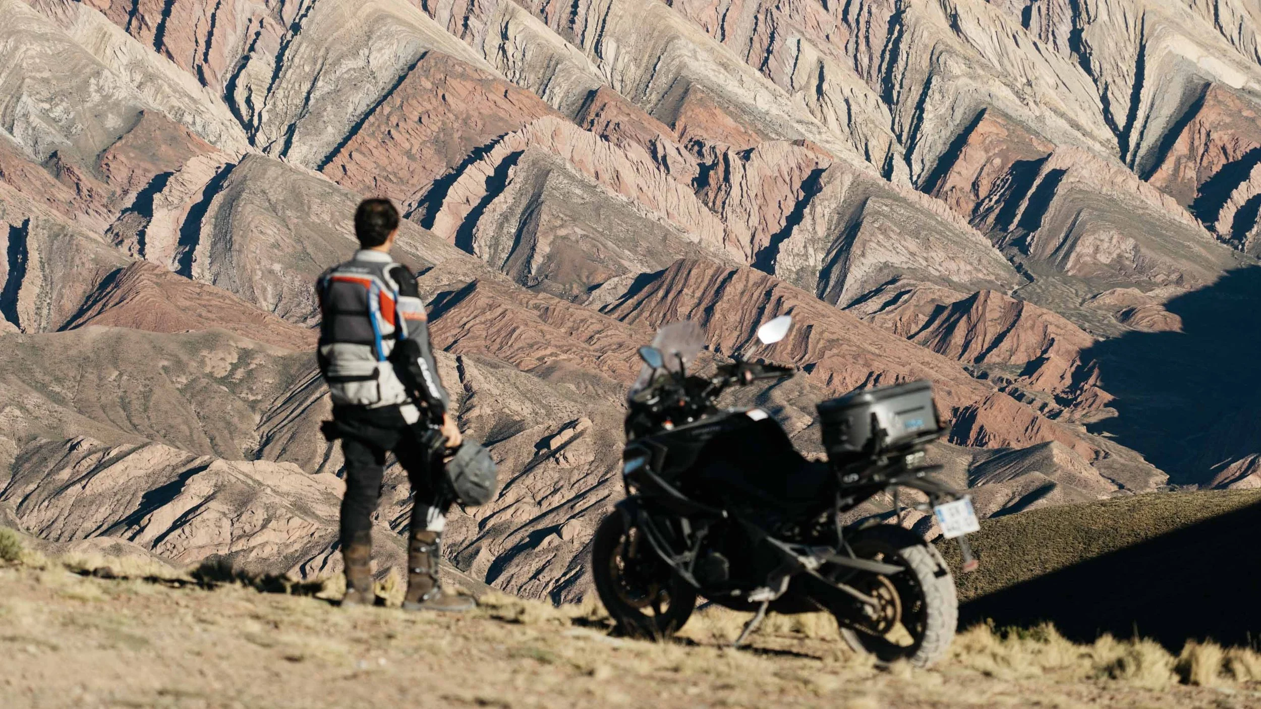 A CF Moto rider in motion against the backdrop of the Cerro de los Siete Colores mountains in Purmamarca, Argentina.
