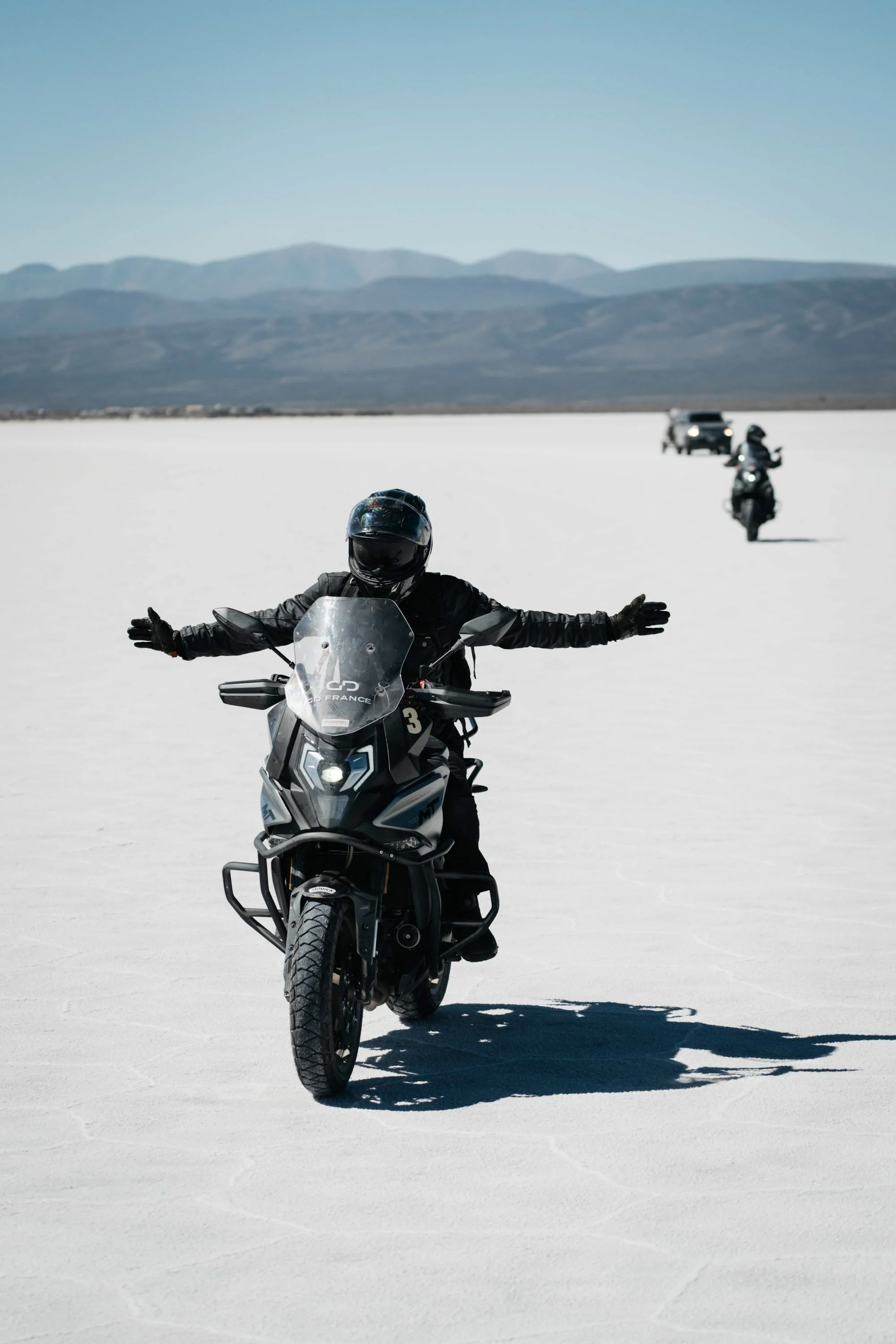 A CF Moto rider celebrating arrival at the Salinas Grandes salt flats in Jujuy, Argentina, with arms outstretched.