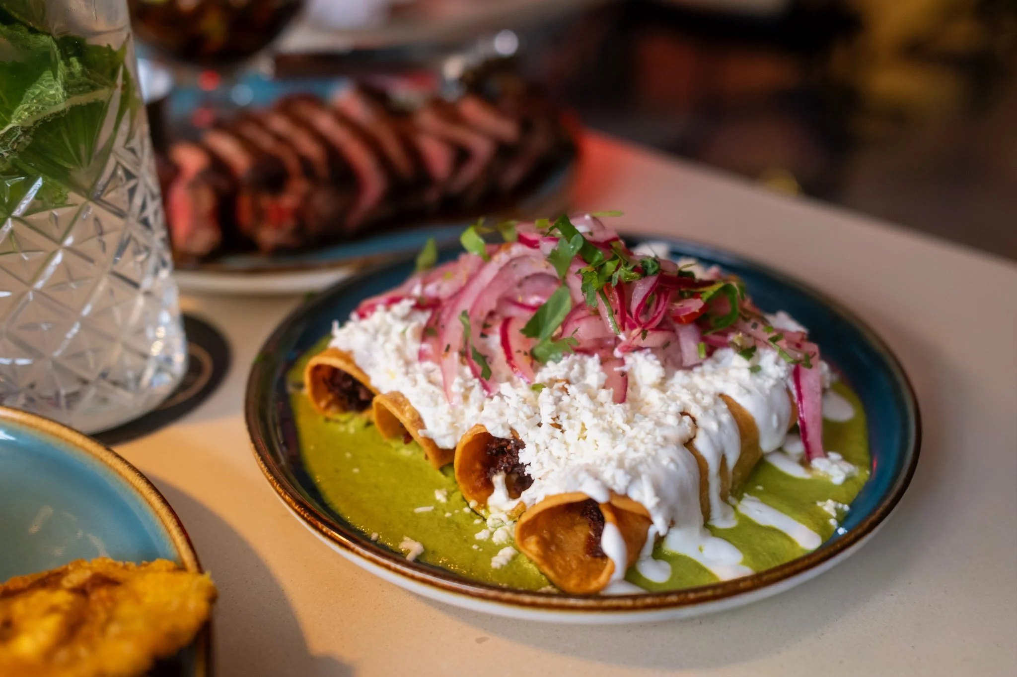 Plate of Mexican enchiladas topped with sour cream, cheese, and sliced onions and herbs, with green sauce underneath.