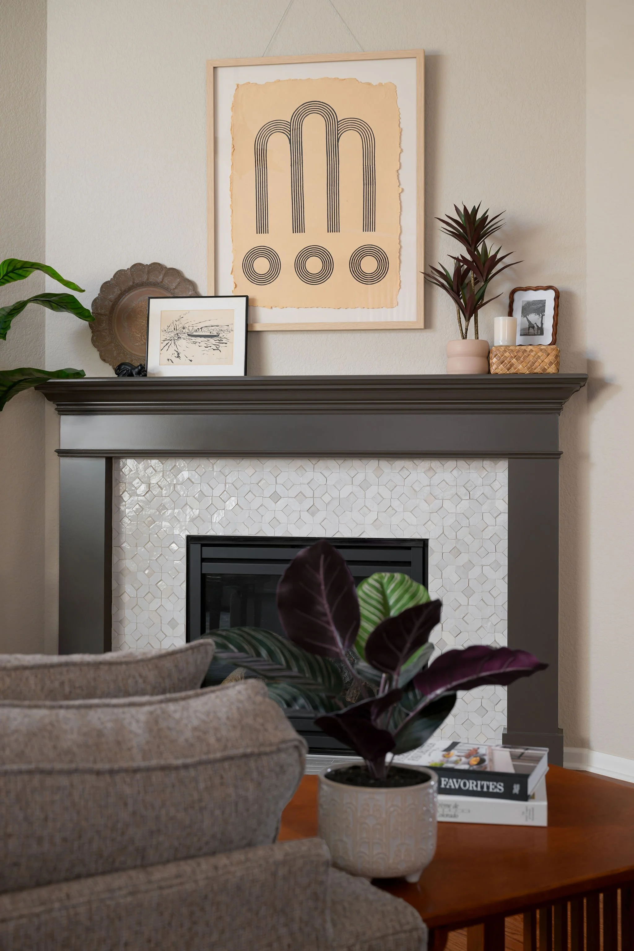 Living room with fireplace, decorative plants, framed artwork, and books on a wooden table.