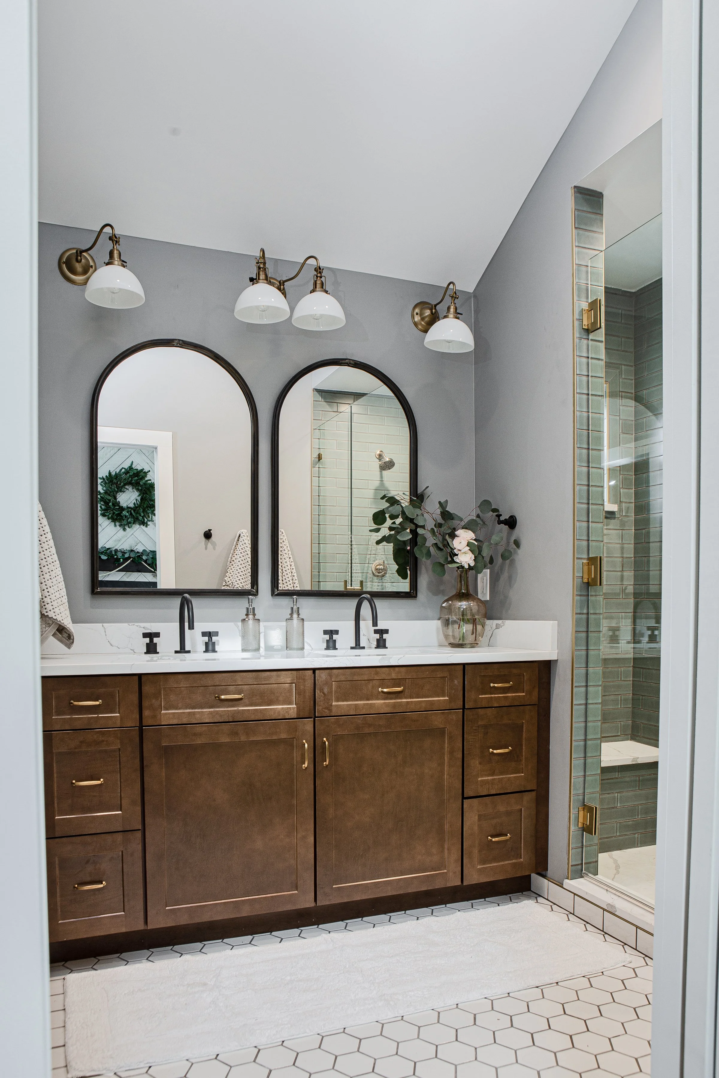 A modern bathroom with a double vanity, two mirrors, and a shower with green tile walls.