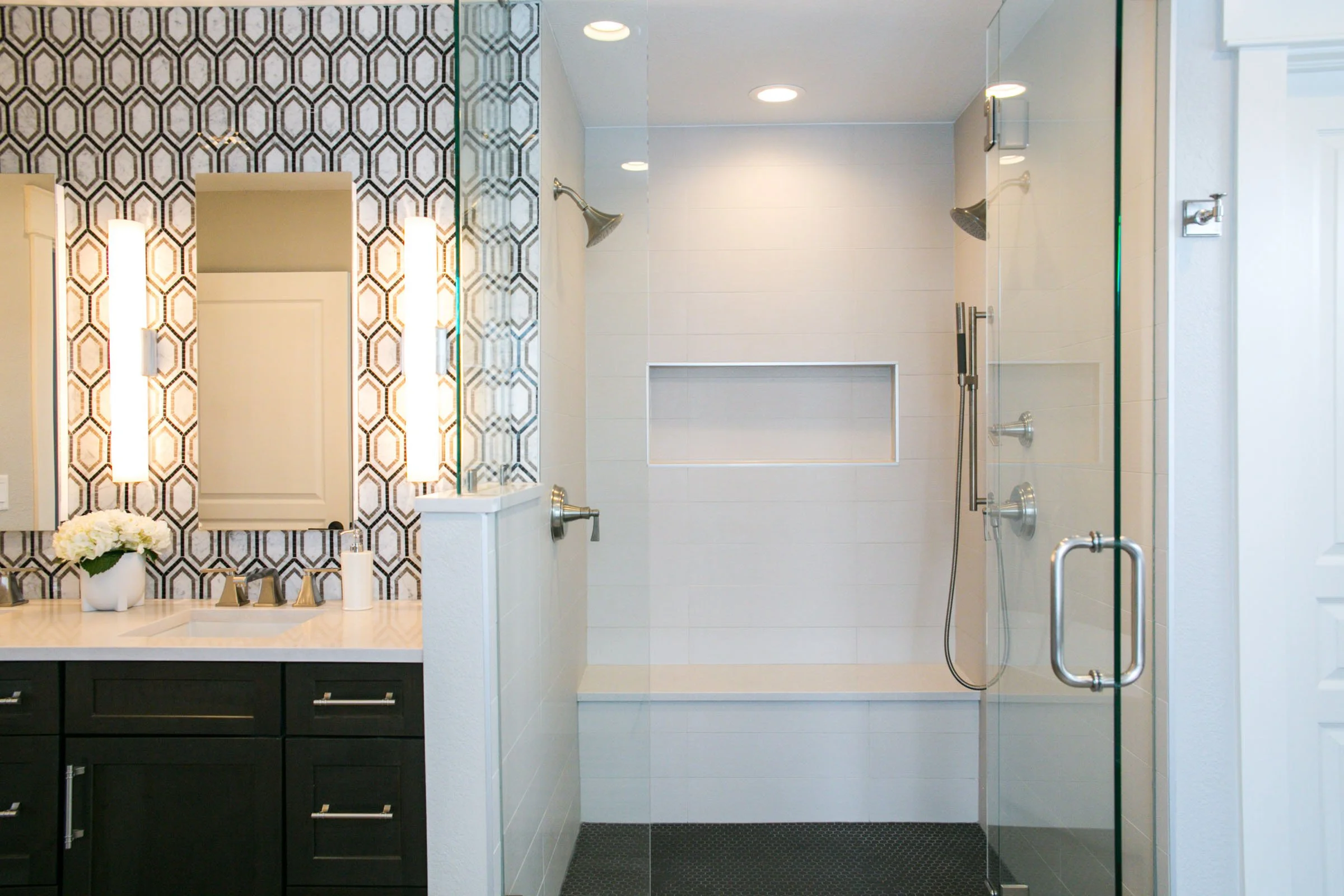 Modern bathroom with a glass shower enclosure, a built-in shower niche, and a vanity area with a mirror, lights, and a flower arrangement.