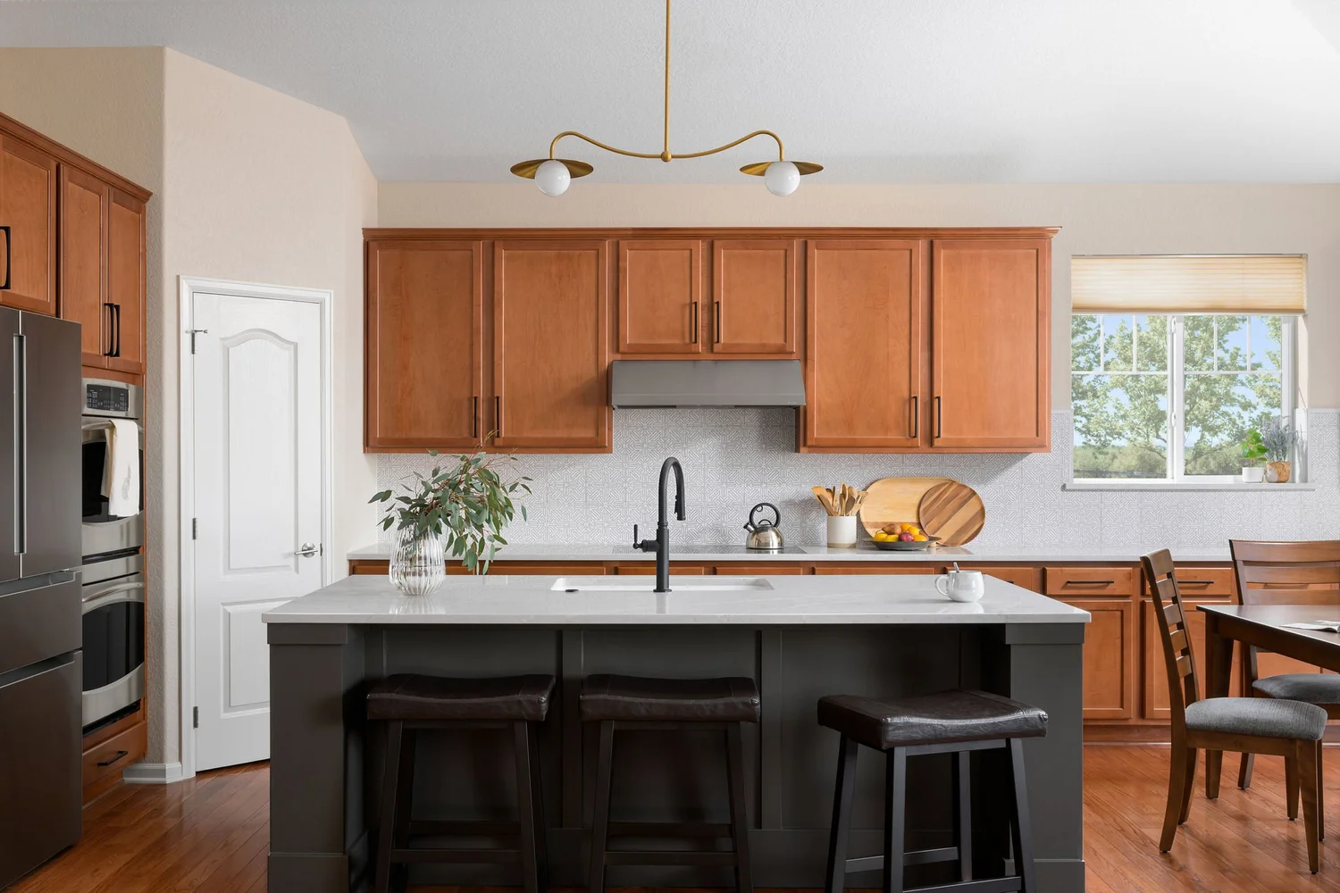 Renovated kitchen with the original warm wood perimeter cabinets kept in place, a new black island with a white quartz top, black counter stools, and a brass pendant light