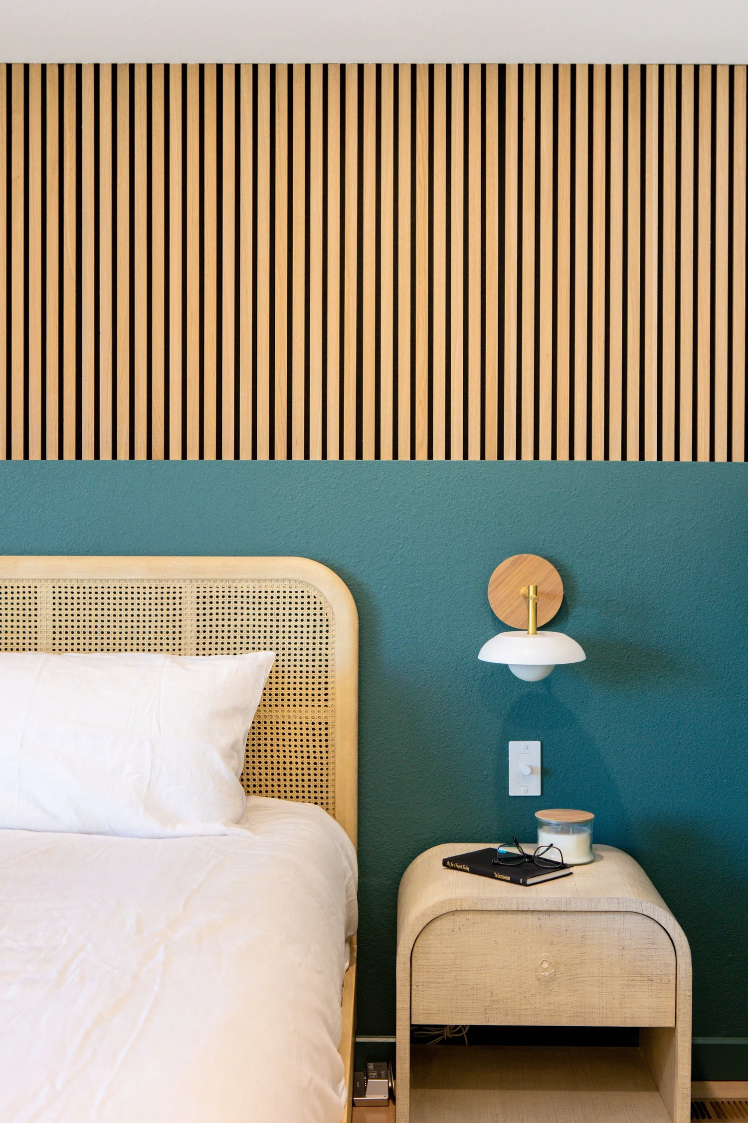 Primary bedroom at the Squiggle Squiggle Dot Dot project in Arvada, a teal wall with a caned headboard and a brass sconce