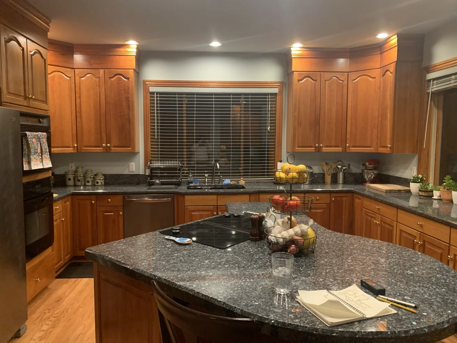 Kitchen before renovation with red oak cabinets and a curved granite island