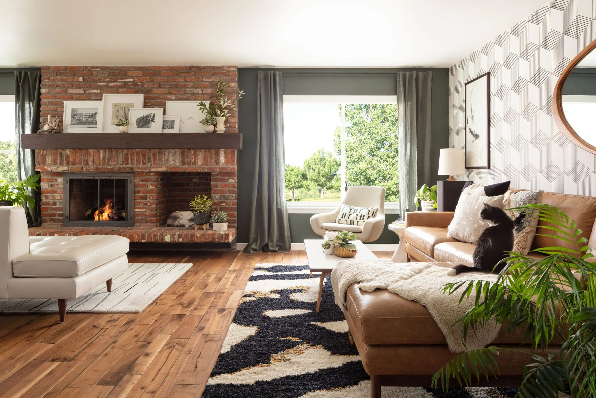 Cozy living room with brick fireplace, modern furniture, large window showing green trees, and a black and white cat sitting on a tan leather sofa.