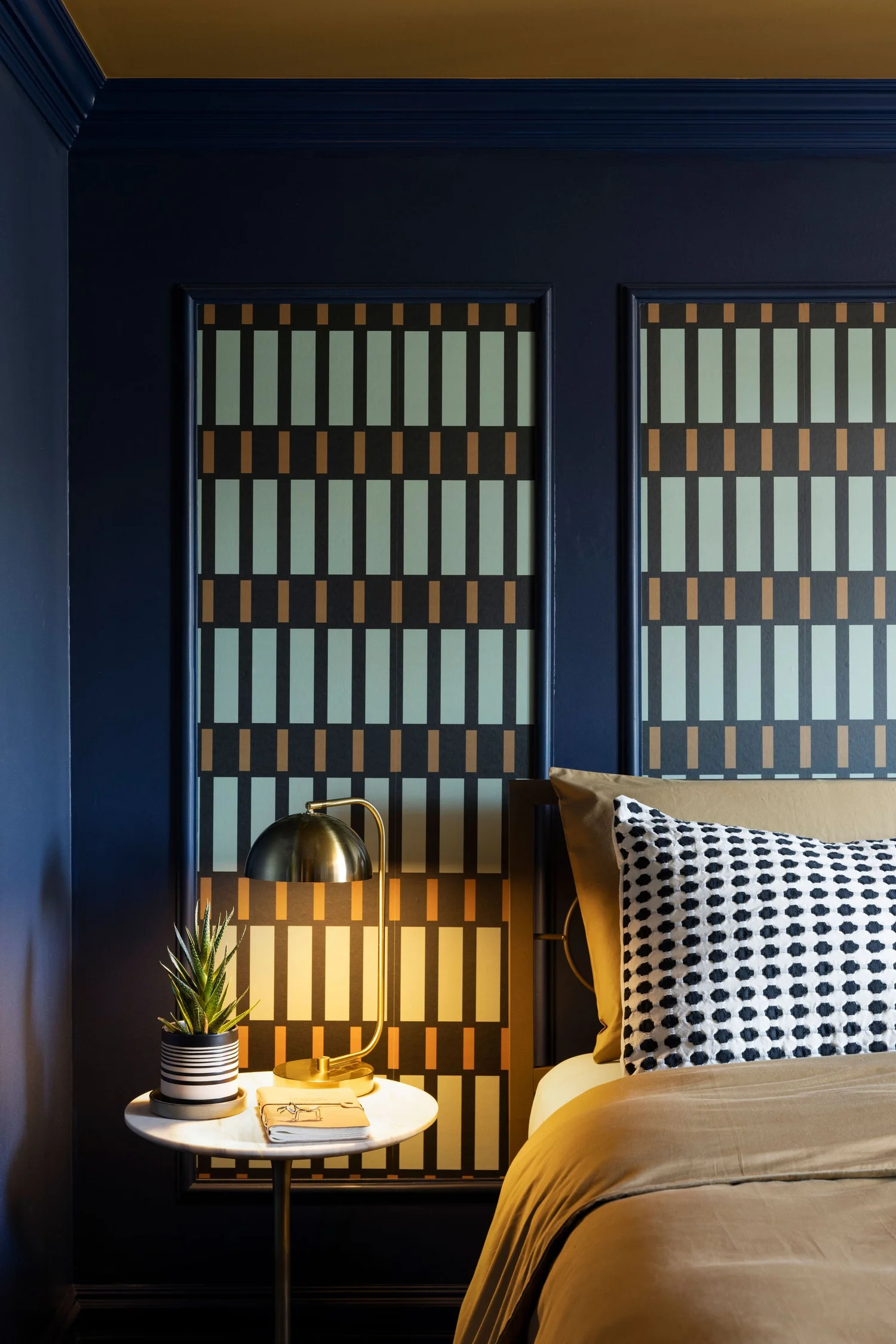 Geometric wallpaper panels set inside custom trim behind the bed